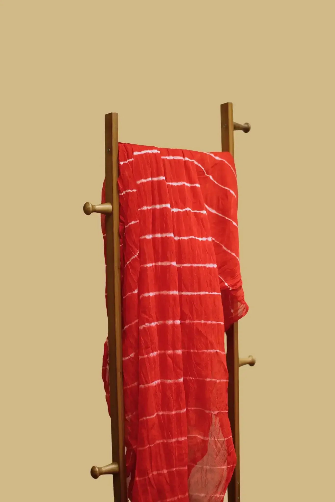 Red tie-dye cotton dupatta with white stripes draped on a wooden ladder against beige background
