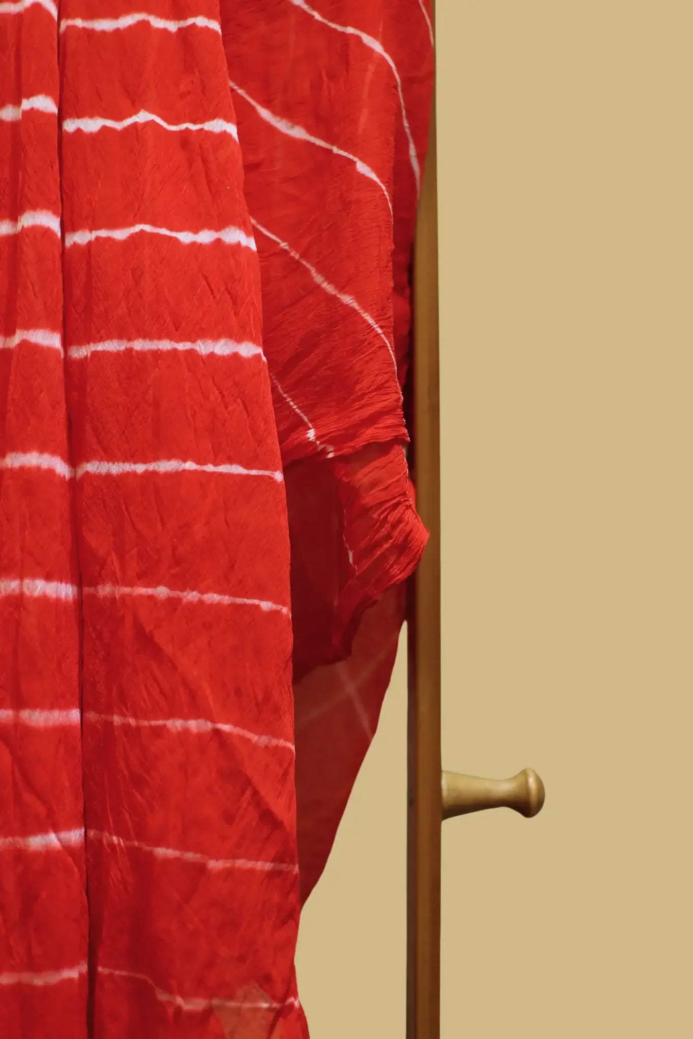 Red handloom fabric with white tie-dye stripes draped on a wooden stand