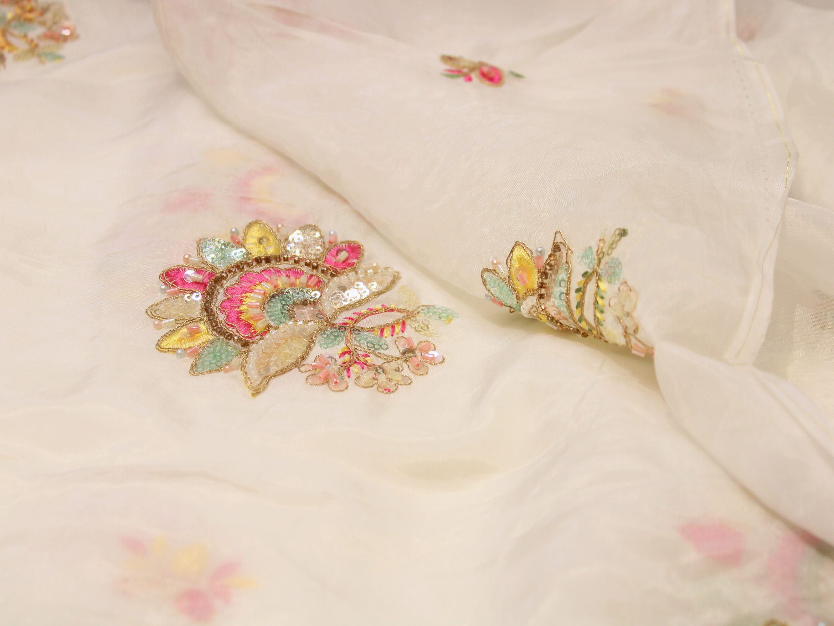 White Indian fabric with pastel floral embroidery and sequins, unstitched textile closeup