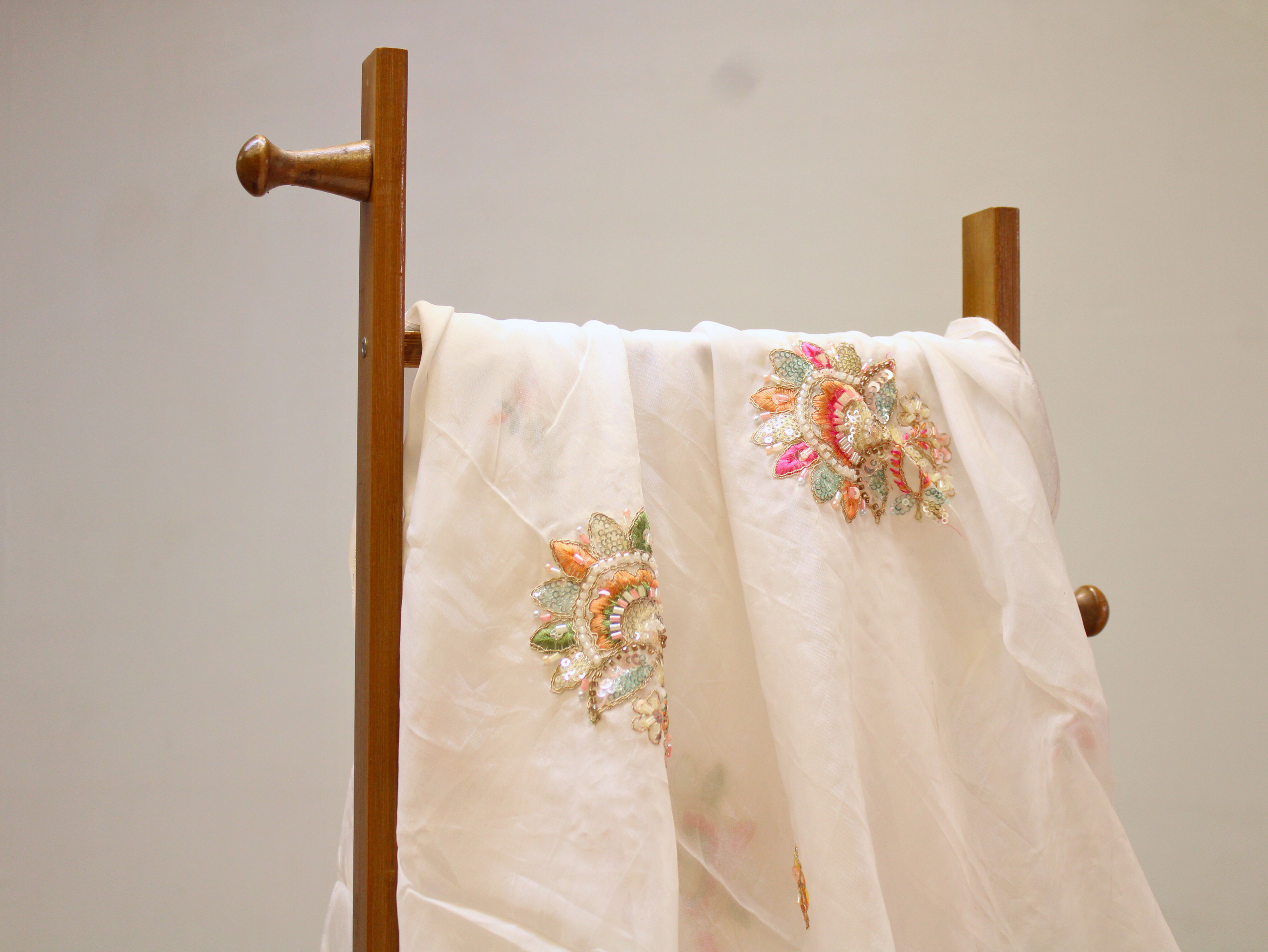White embroidered dupatta with colorful floral embellishments draped on wooden stand