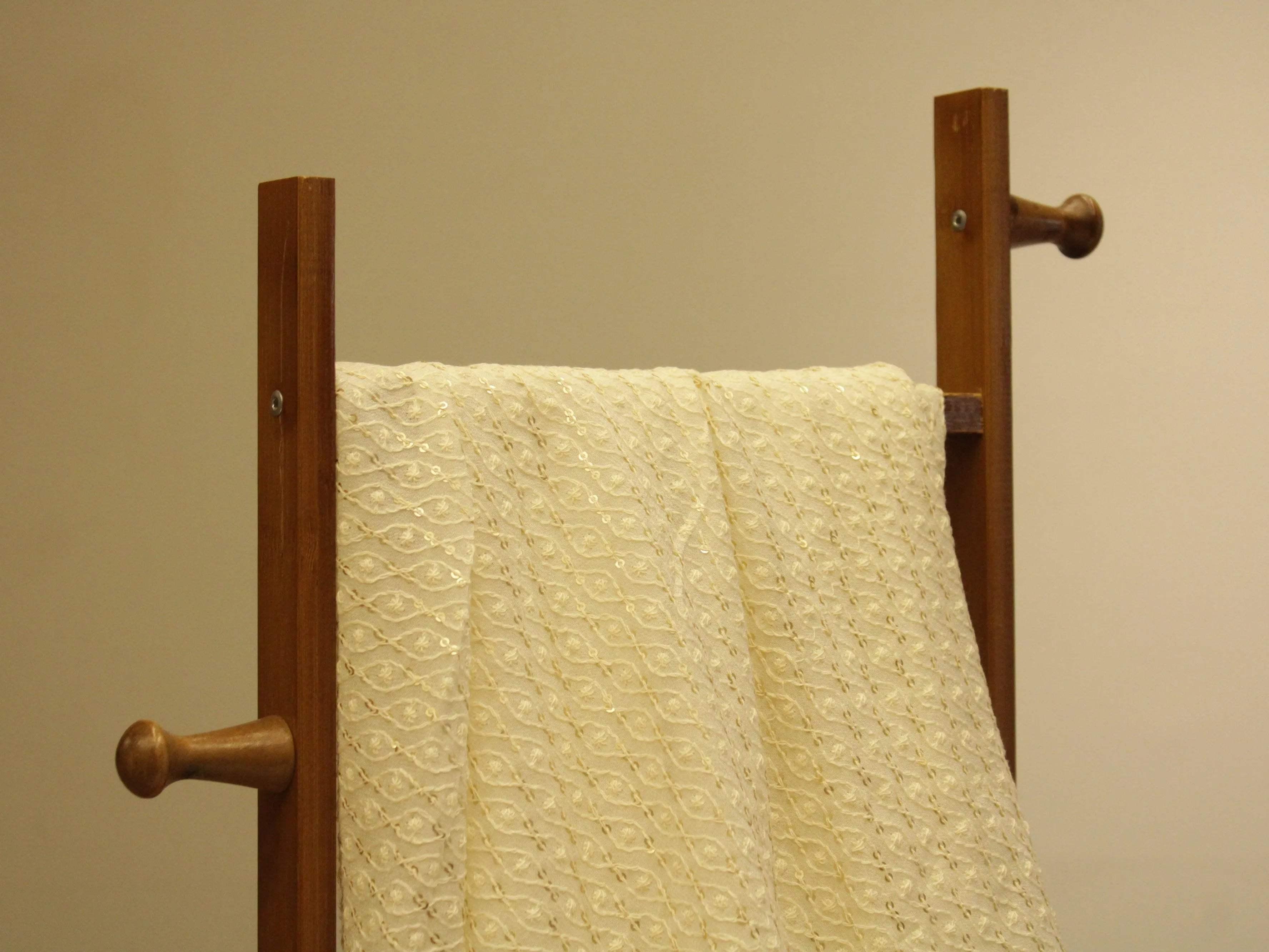 Cream embroidered Indian fabric with sequins draped over a wooden stand
