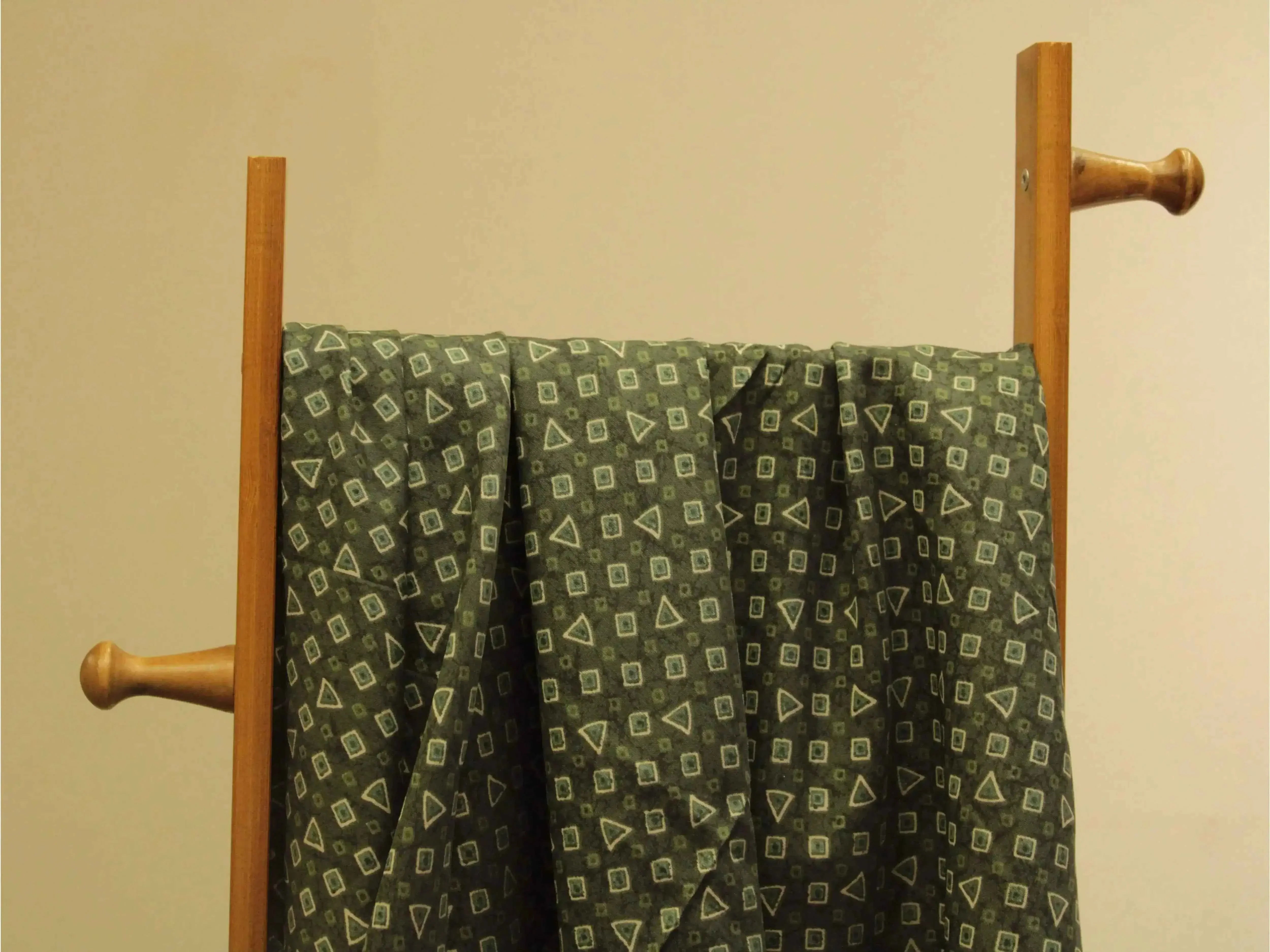Green Indian cotton fabric with geometric print draped over a wooden stand