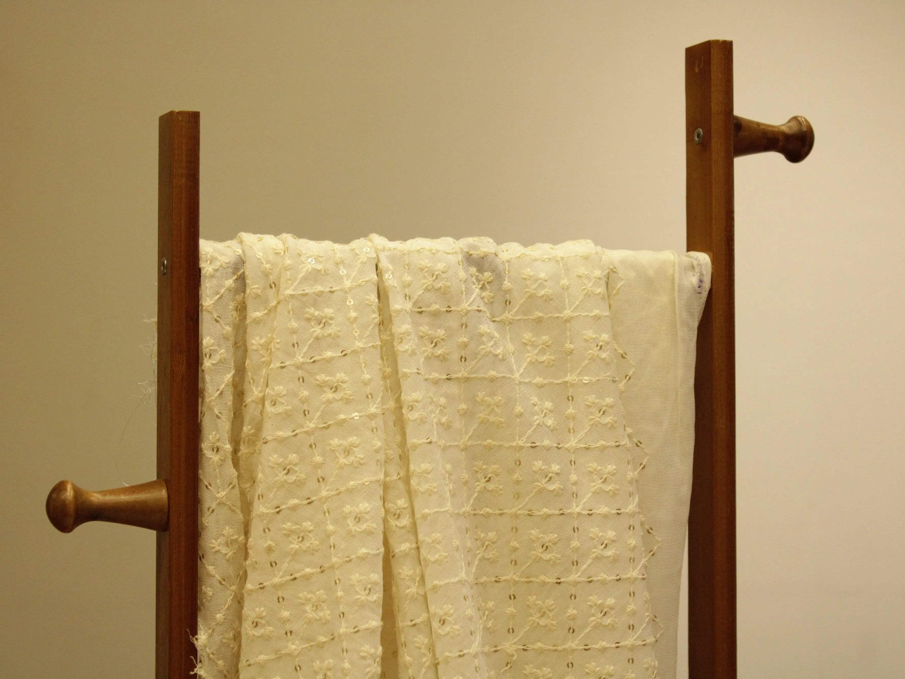 White georgette Lucknawi thread and sequin work fabric draped on a wooden stand