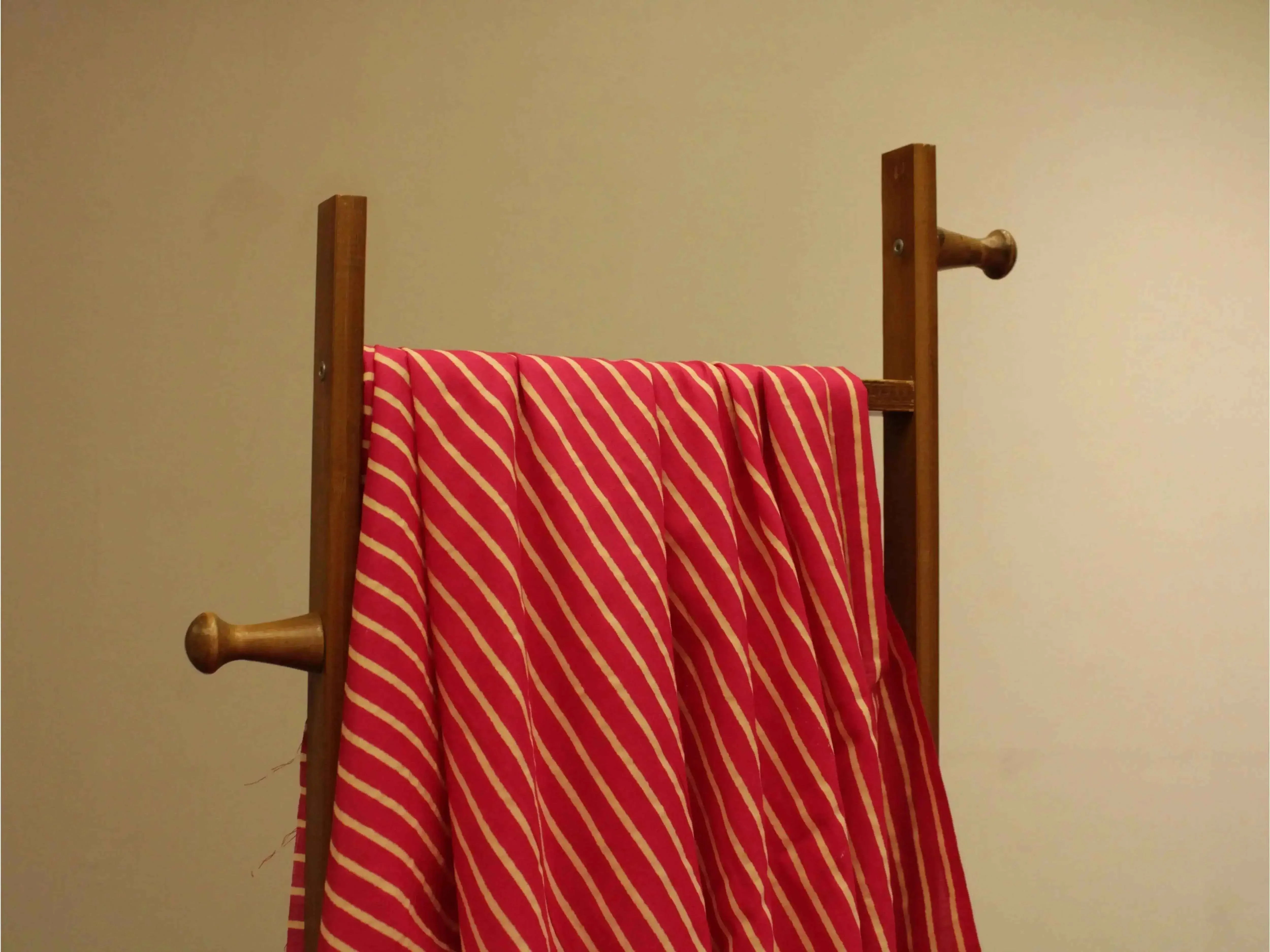 Red cotton hand block printed fabric with diagonal white stripes draped on a wooden rack
