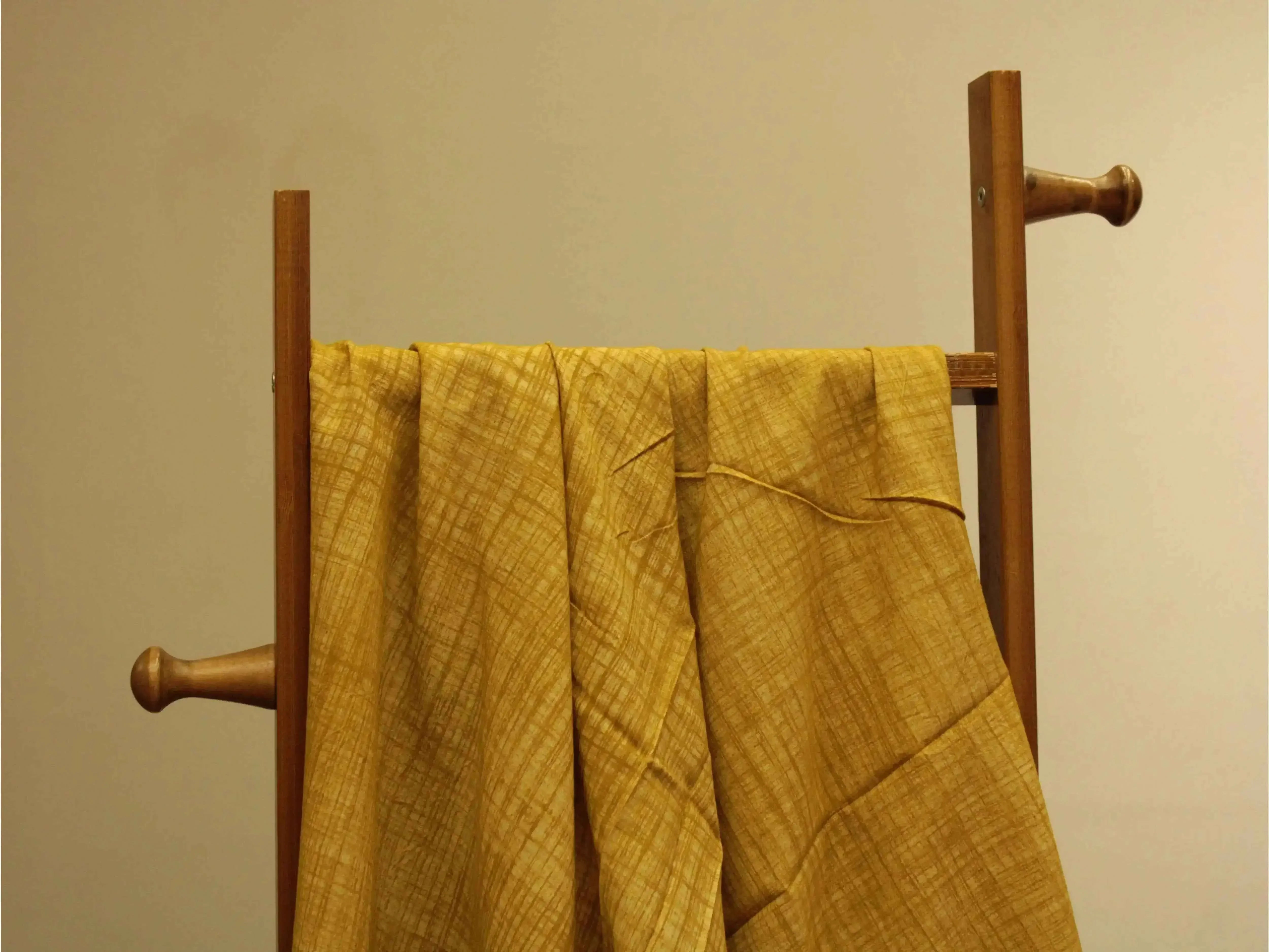 Yellow cotton hand block printed fabric with subtle crisscross pattern on a wooden stand