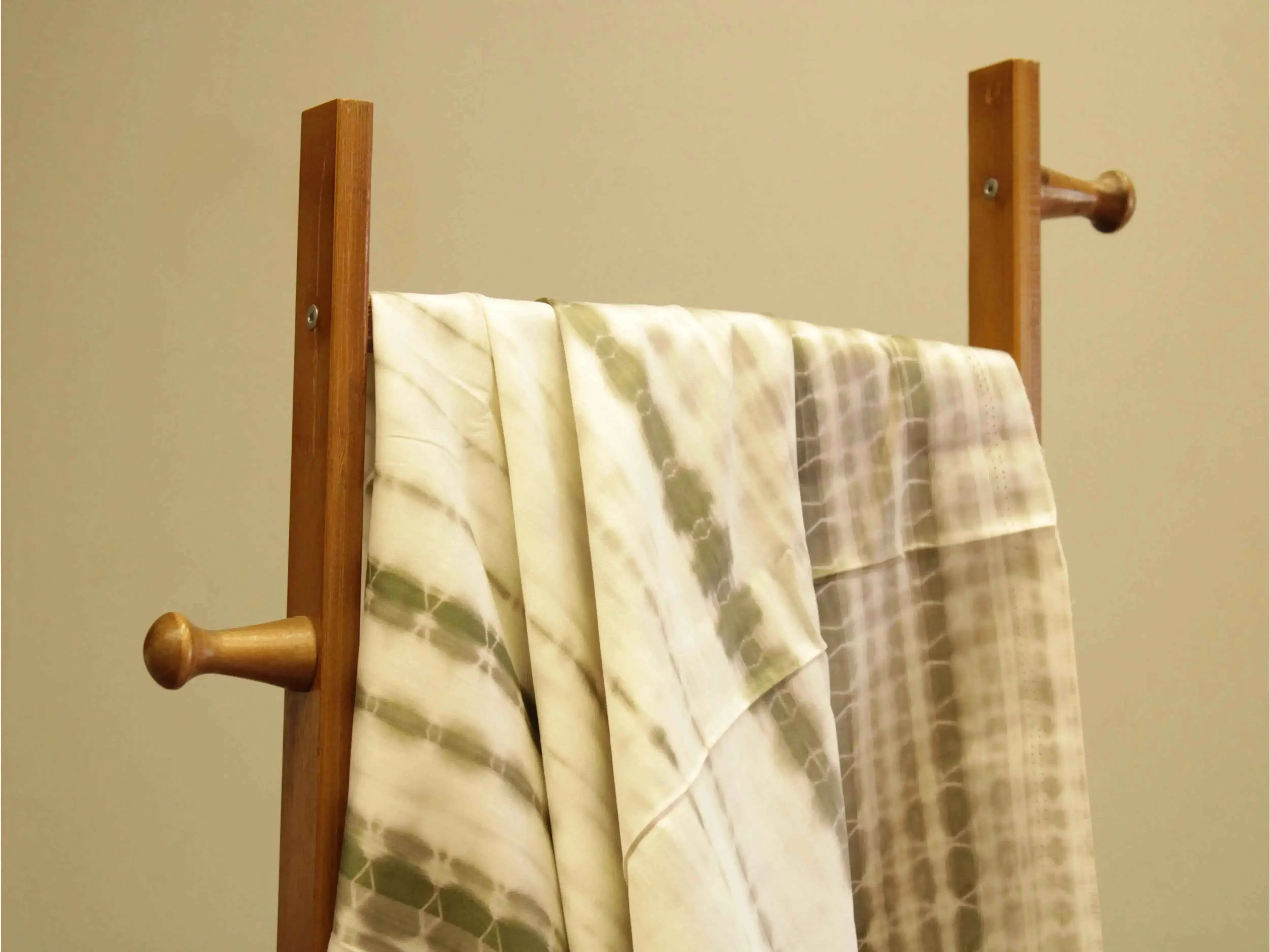 Dusty green cotton satin fabric with shibori print draped on a wooden stand