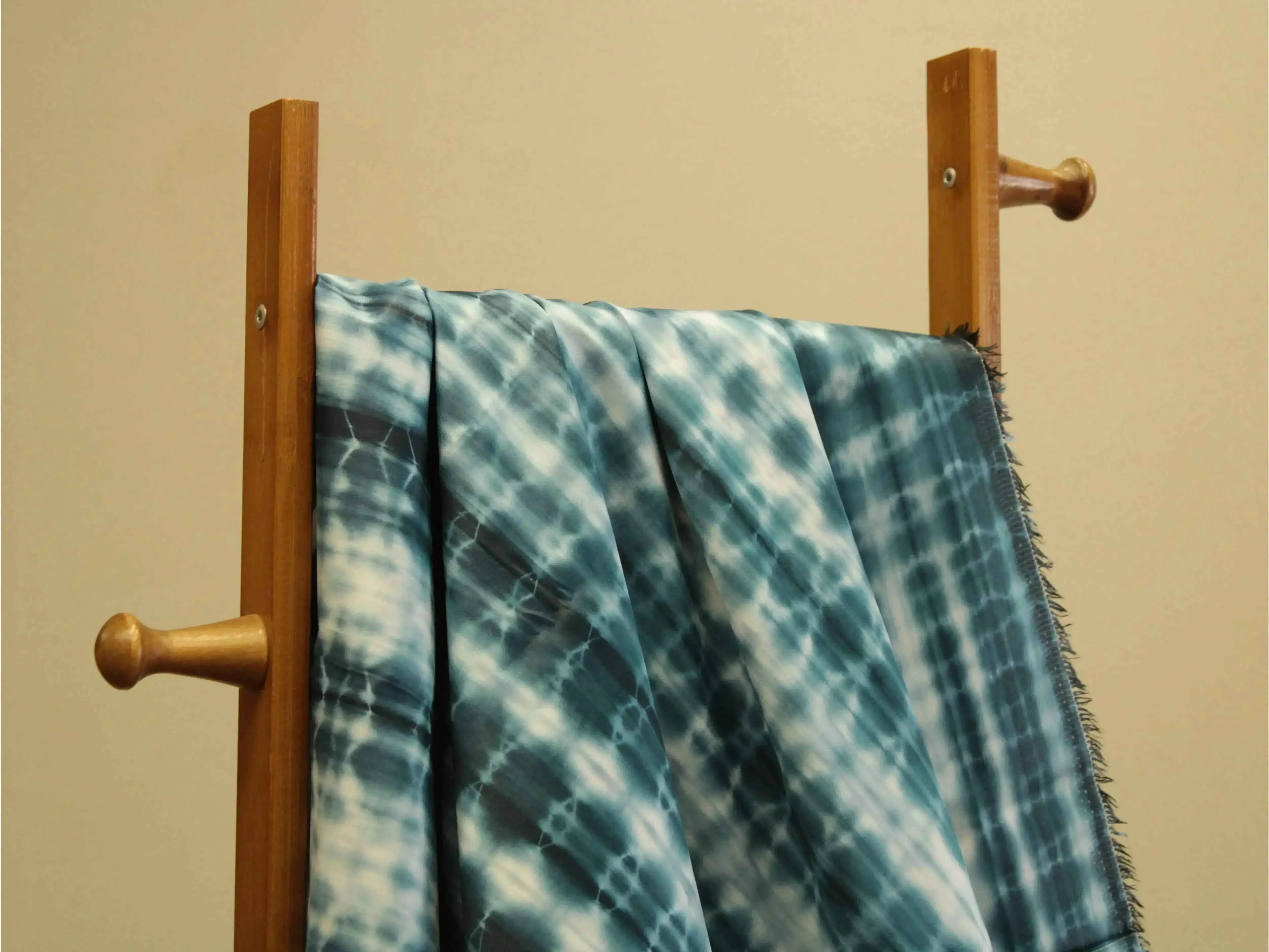 Peacock blue cotton satin shibori printed fabric draped over a wooden rack