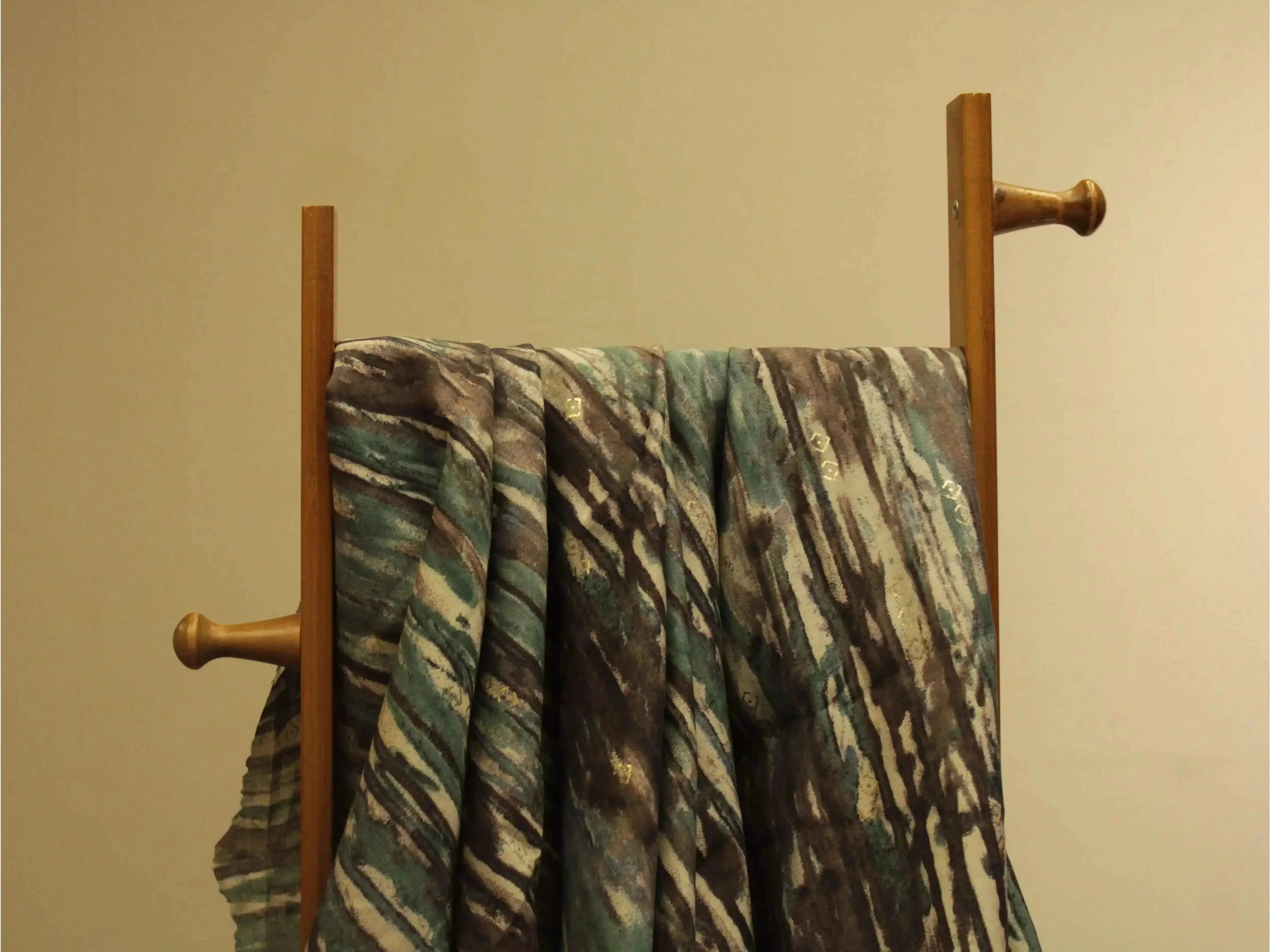 Loud digital print muslin silk fabric with abstract teal and brown pattern draped on a wooden stand