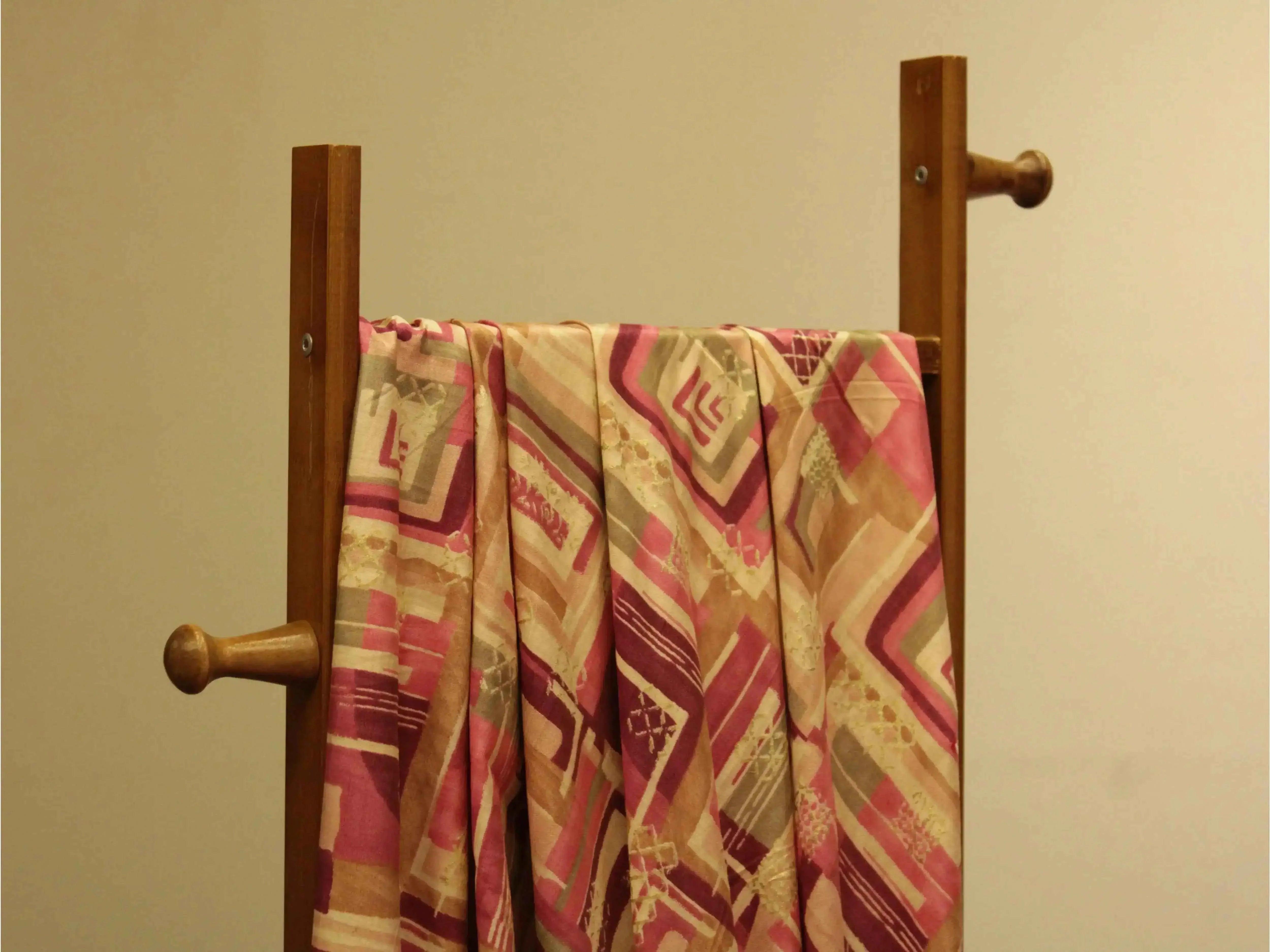 Pink and beige geometric print muslin silk fabric draped on wooden stand