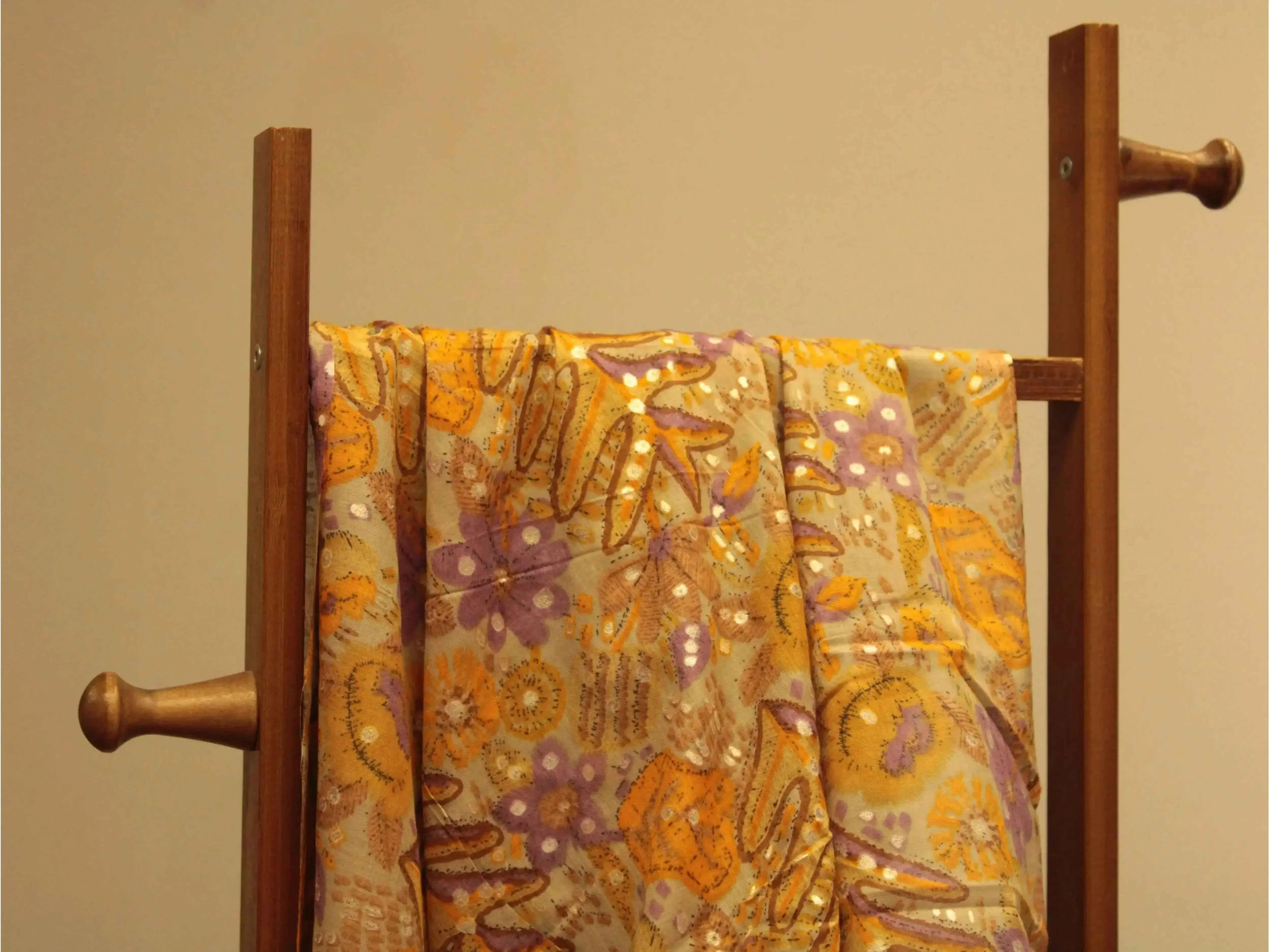Pastel yellow and purple floral cotton fabric draped over a wooden rack, Indian textile print