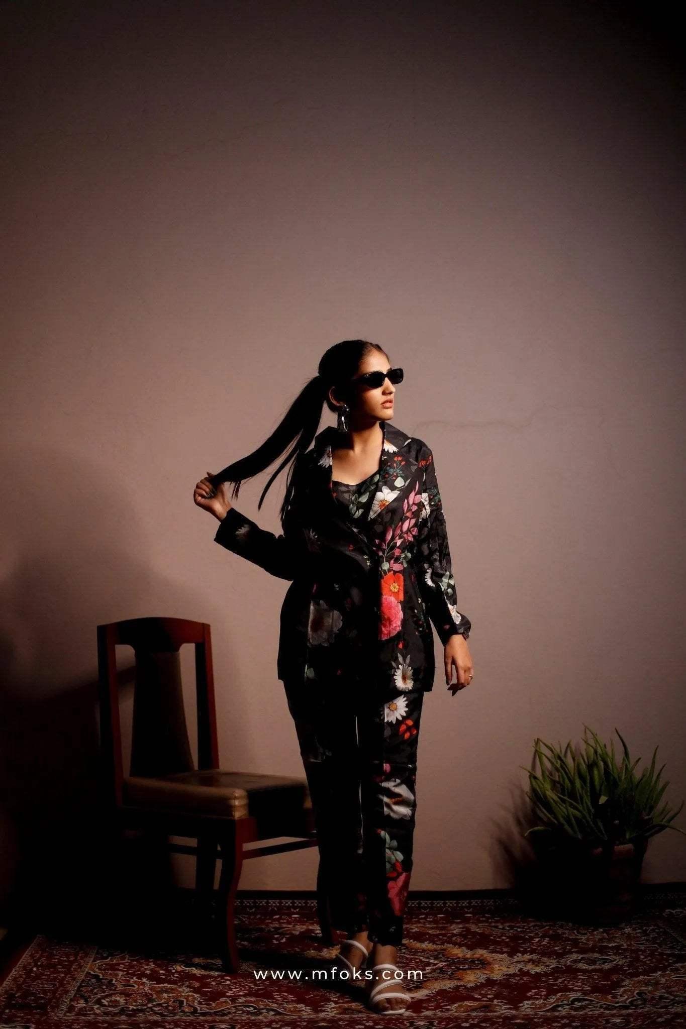 Woman in black floral blazer and pants co-ord set, wearing sunglasses, posing indoors