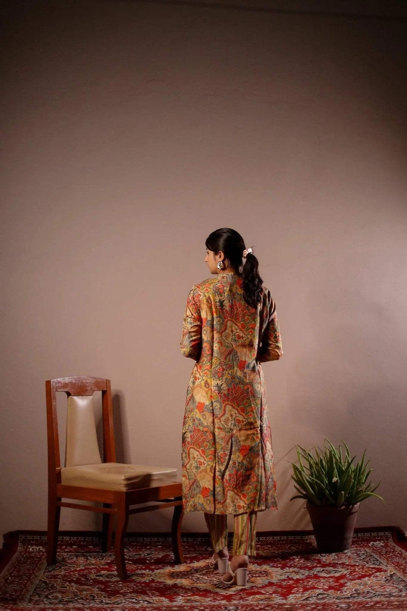 Woman wearing printed blazer and pant co-ord set, standing on a patterned carpet near a chair and plant