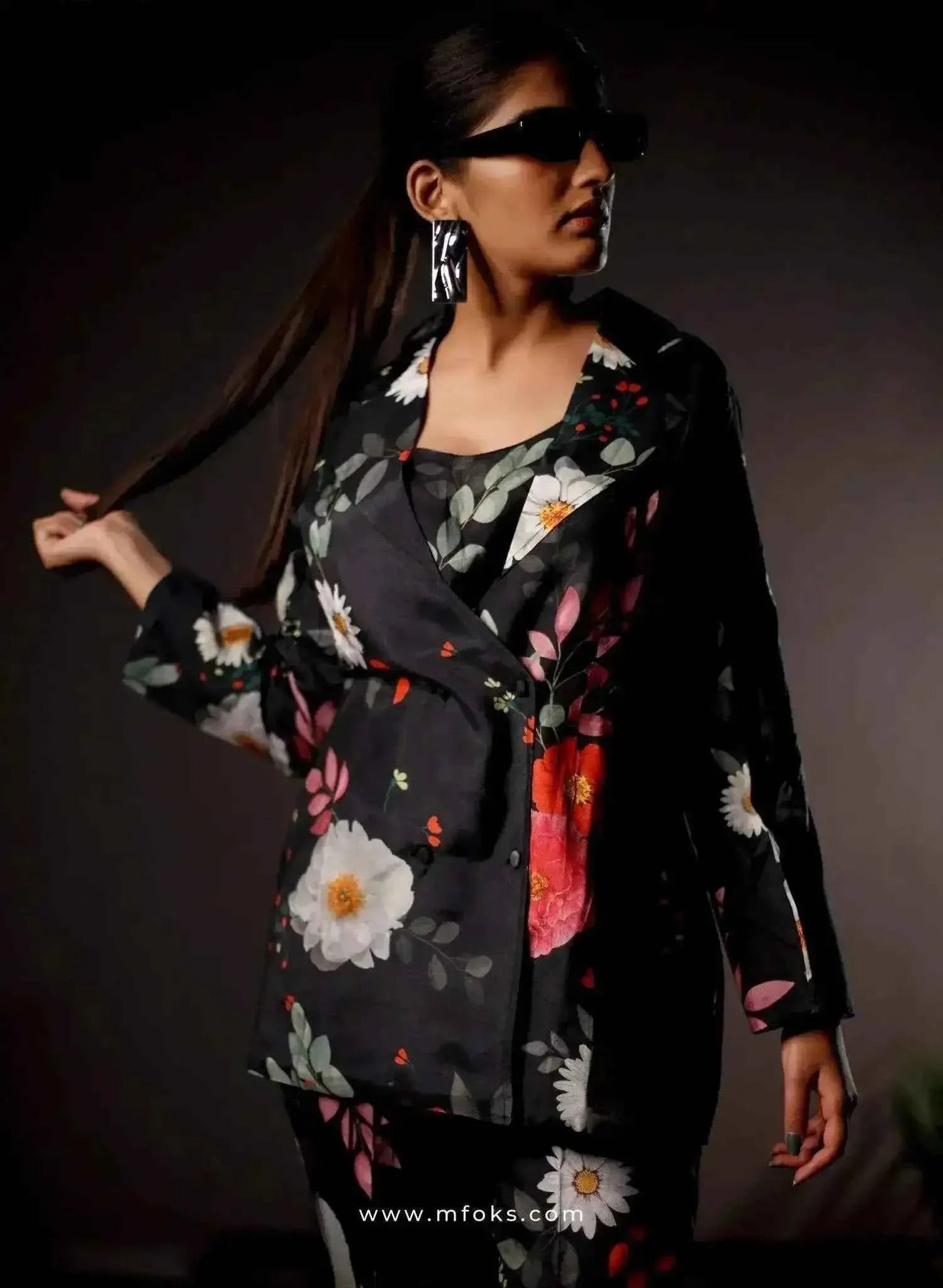 Woman in black floral print blazer and pants set, wearing sunglasses, stylish earrings