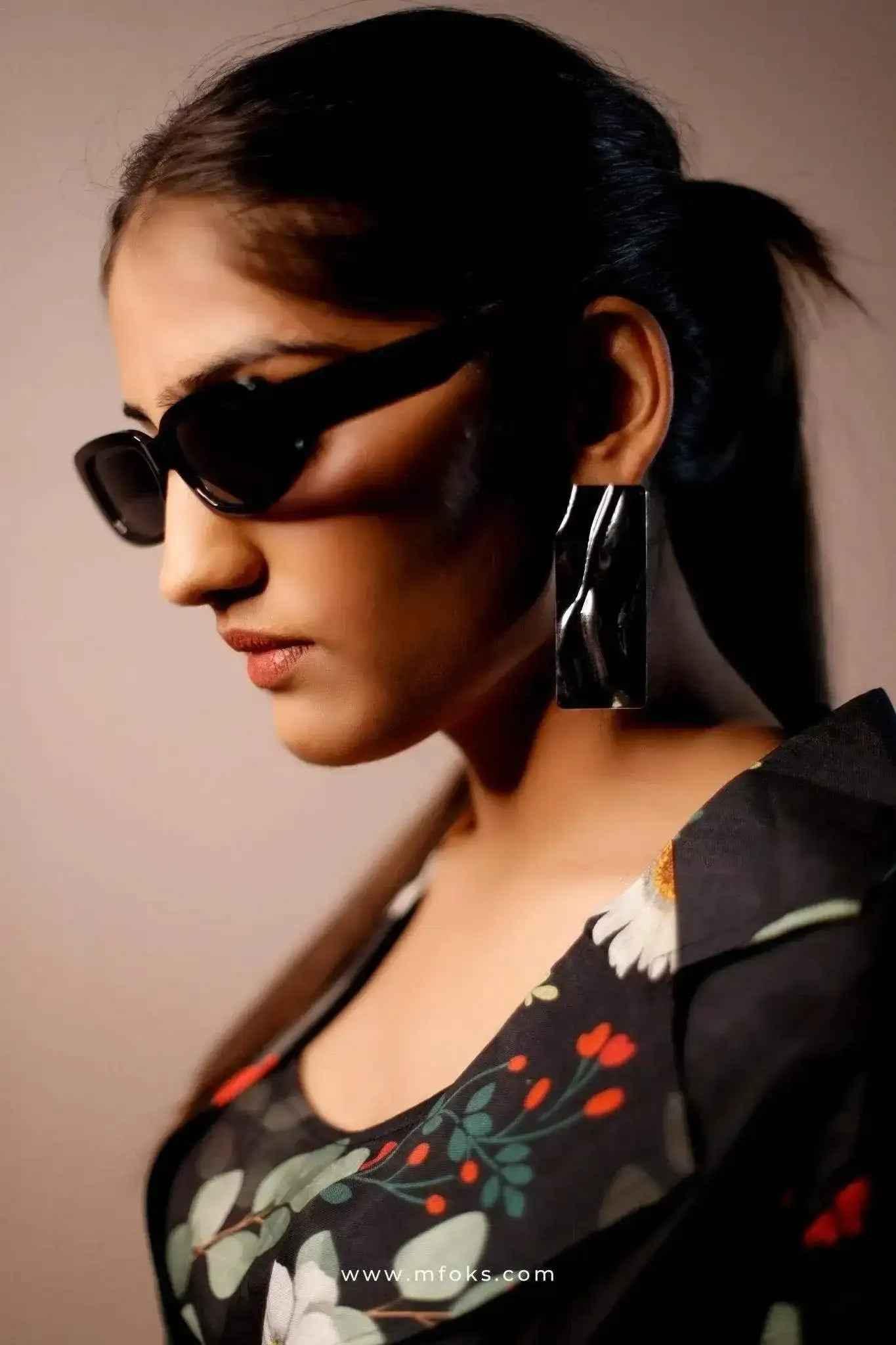 Woman in black floral blazer set, wearing statement earrings and sunglasses