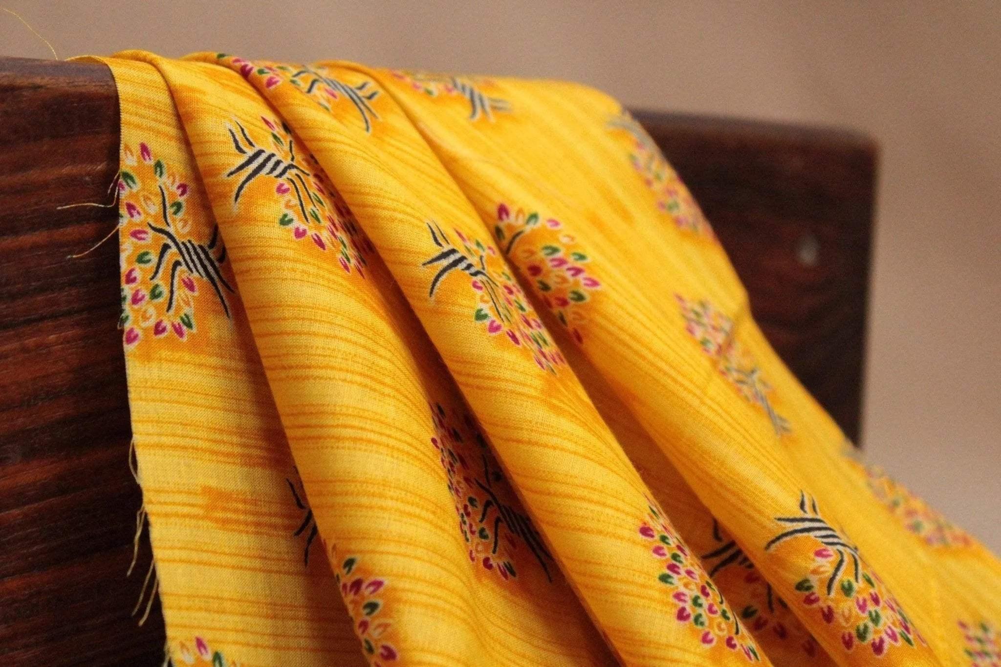 Yellow cotton fabric with buti screen print and small floral motifs draped over wood