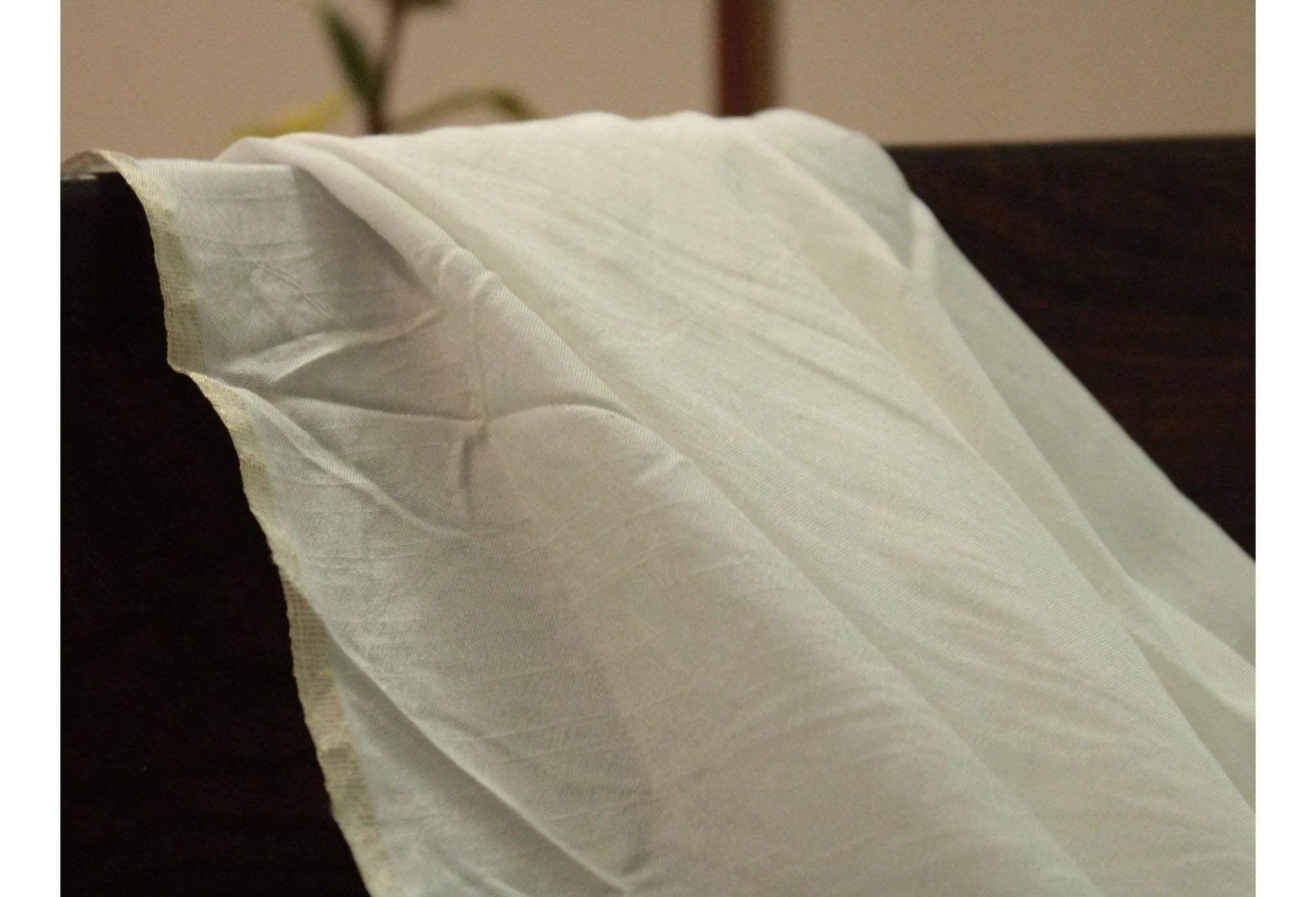 White dyeable Dola silk fabric with a soft, sheer texture draped on a dark surface