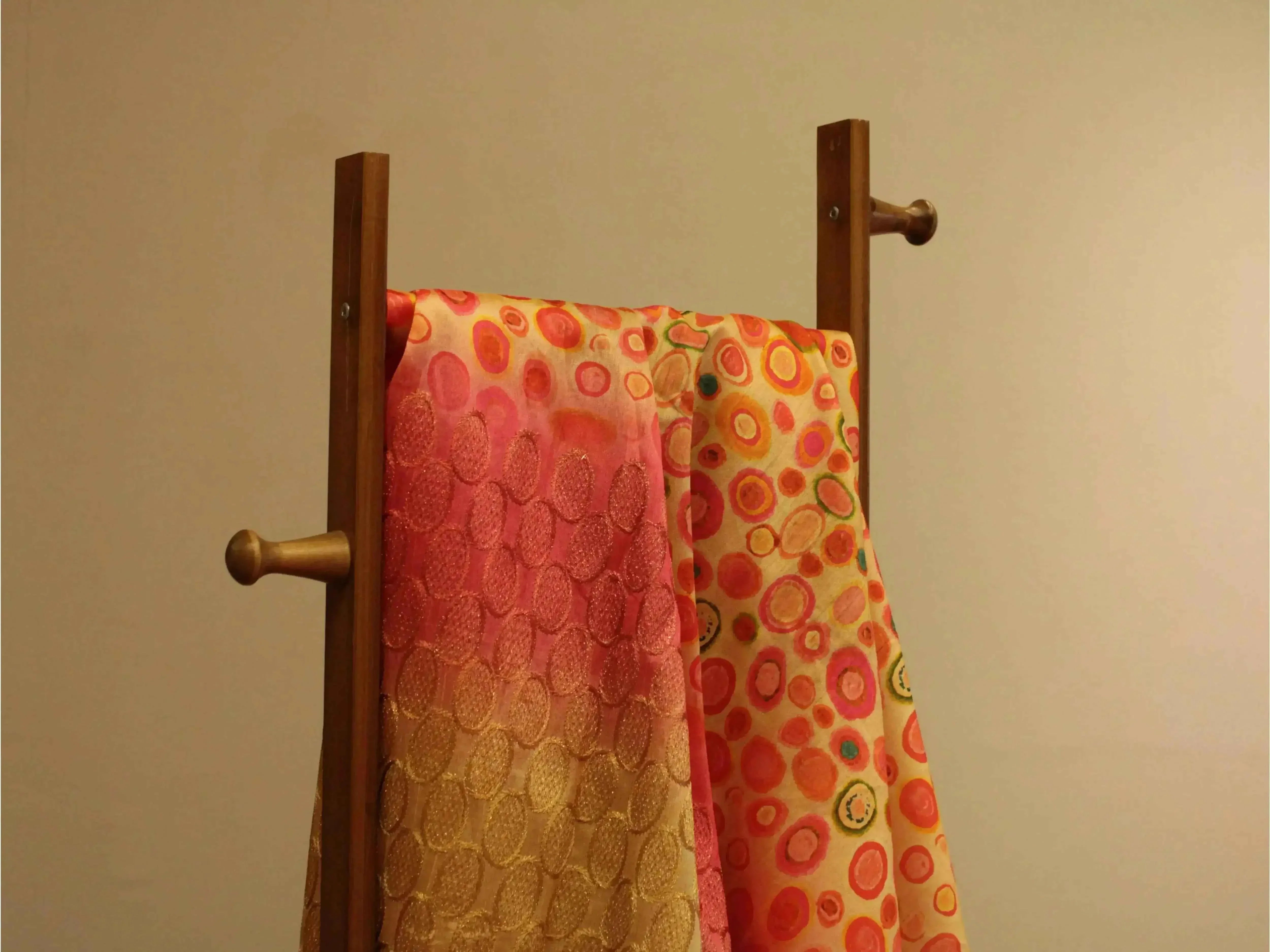 Fine silk fabric with vibrant digital print and panel work in pink and gold hues, draped on a wooden stand.