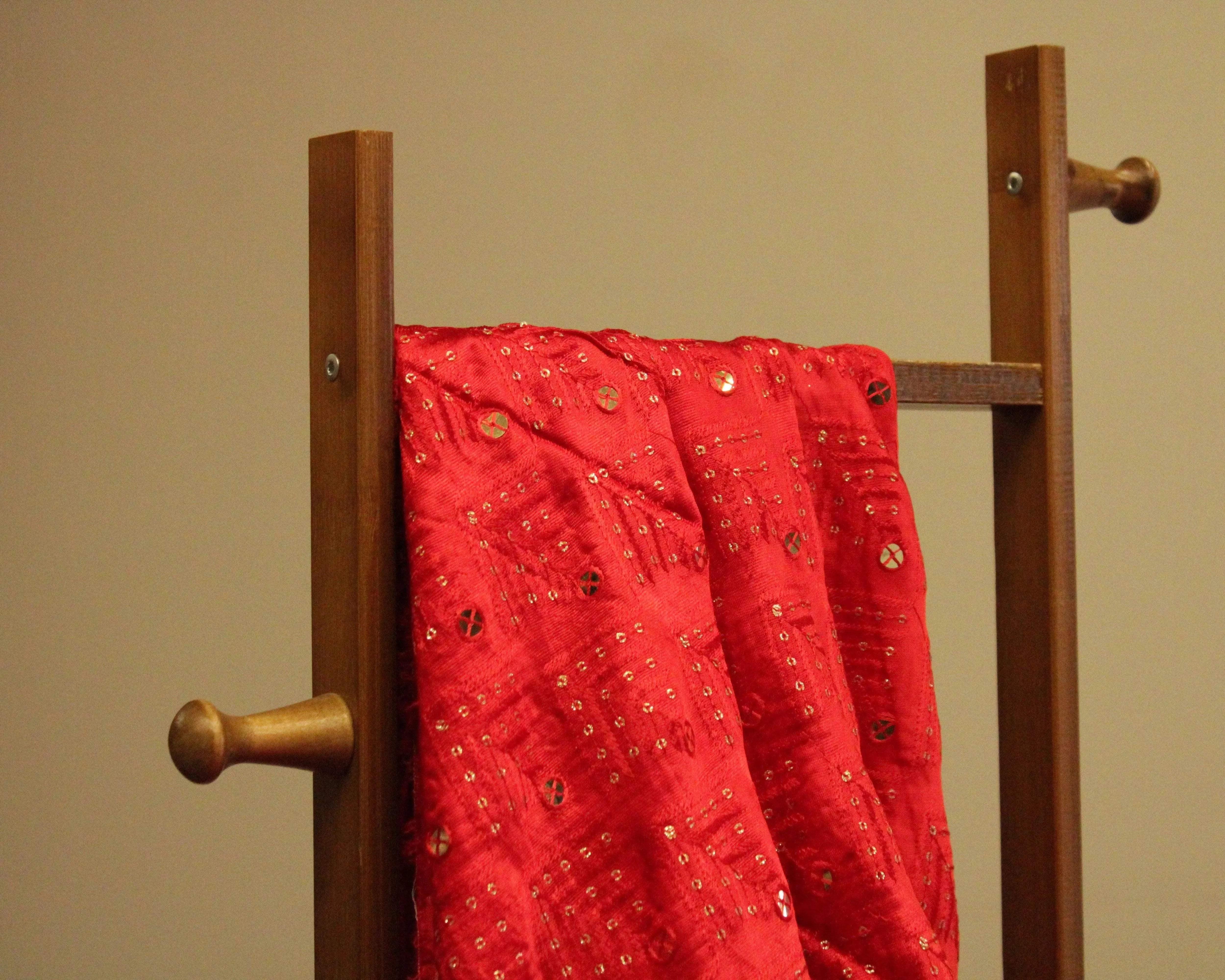 Red gaji silk fabric with thread and paper mirror work draped over wooden stand