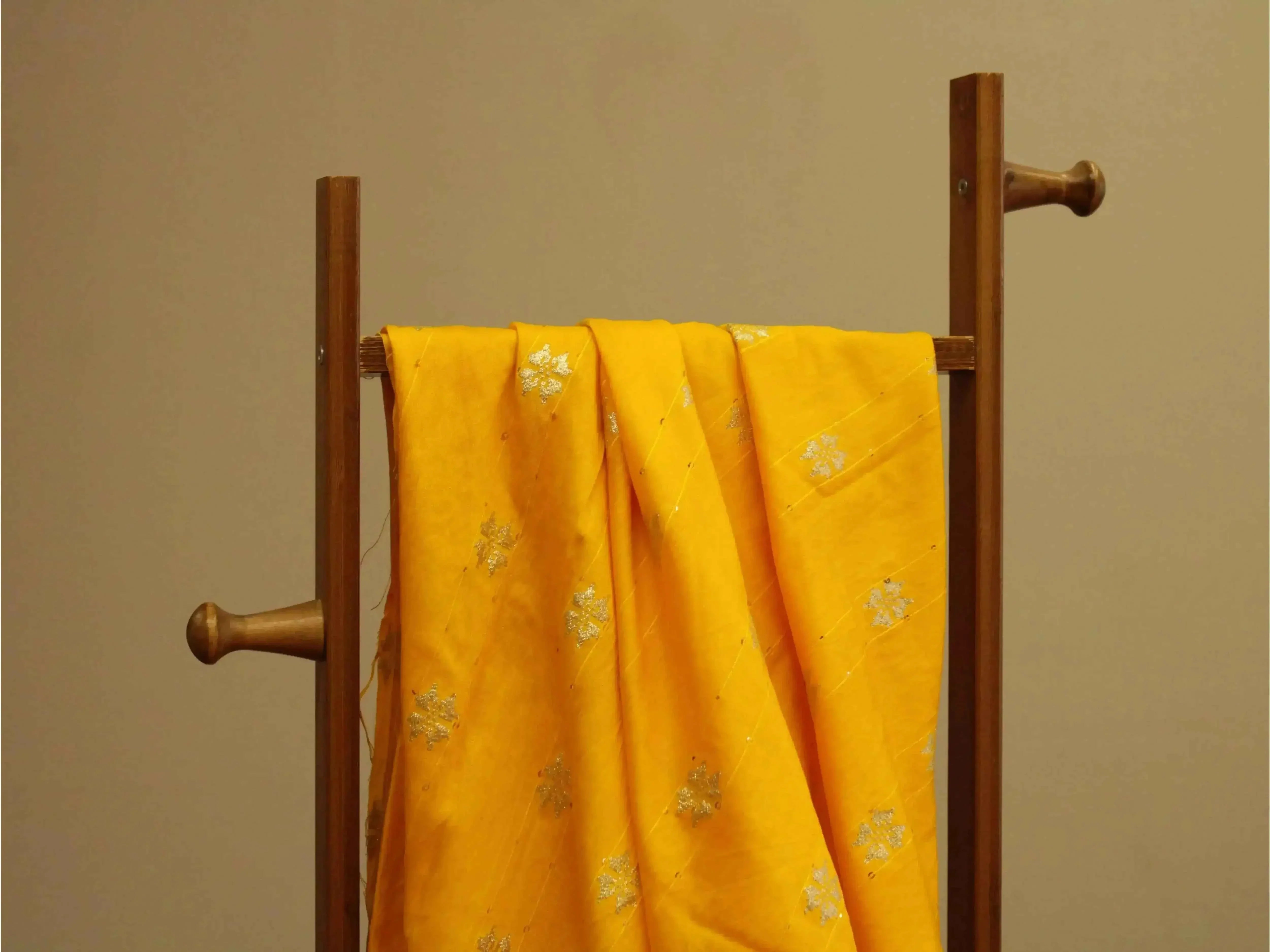 Yellow silk fabric with silver floral embroidery draped on a wooden stand