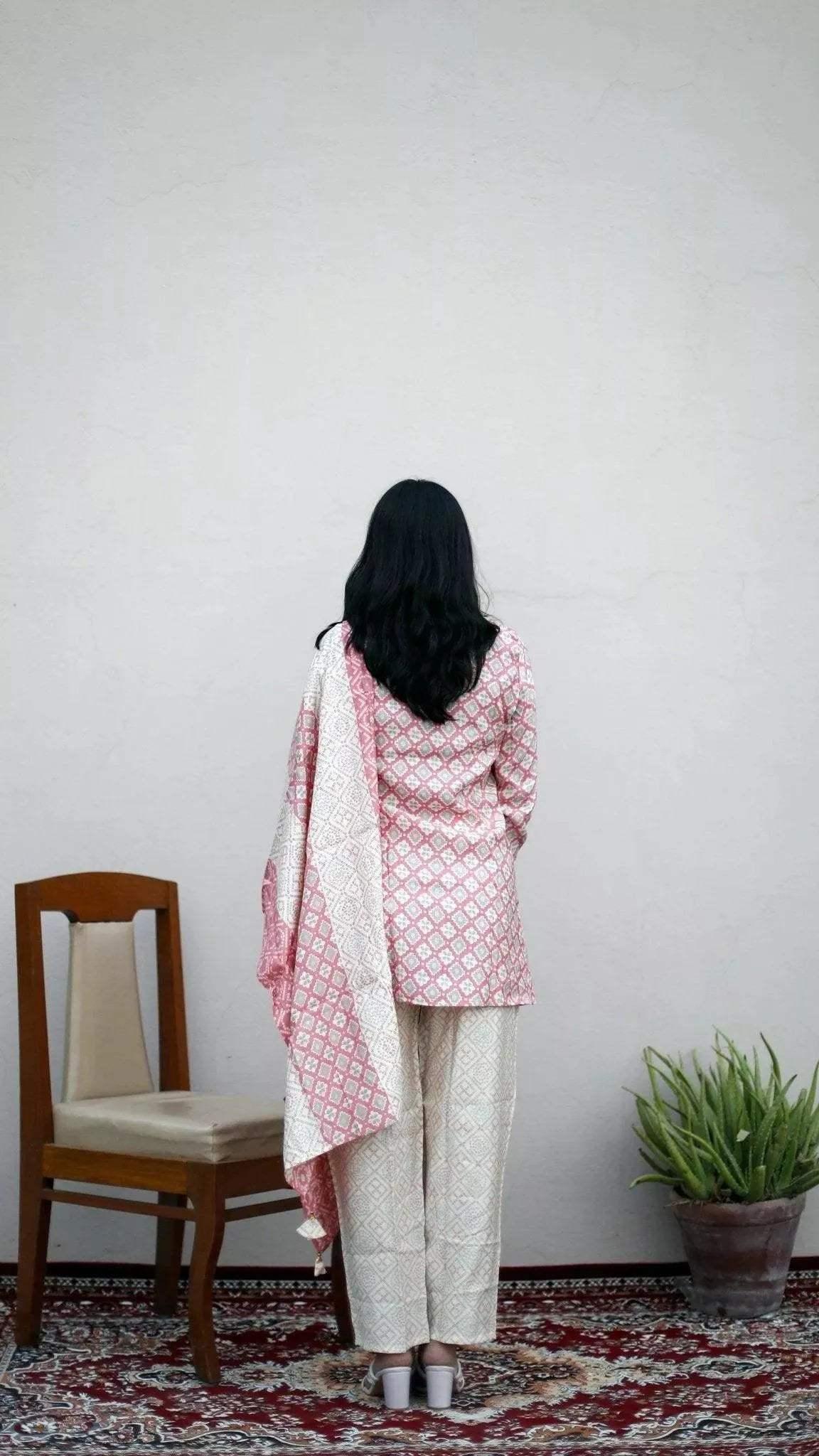 Woman in pink and white muslin long top, dupatta, and pants standing on a patterned rug