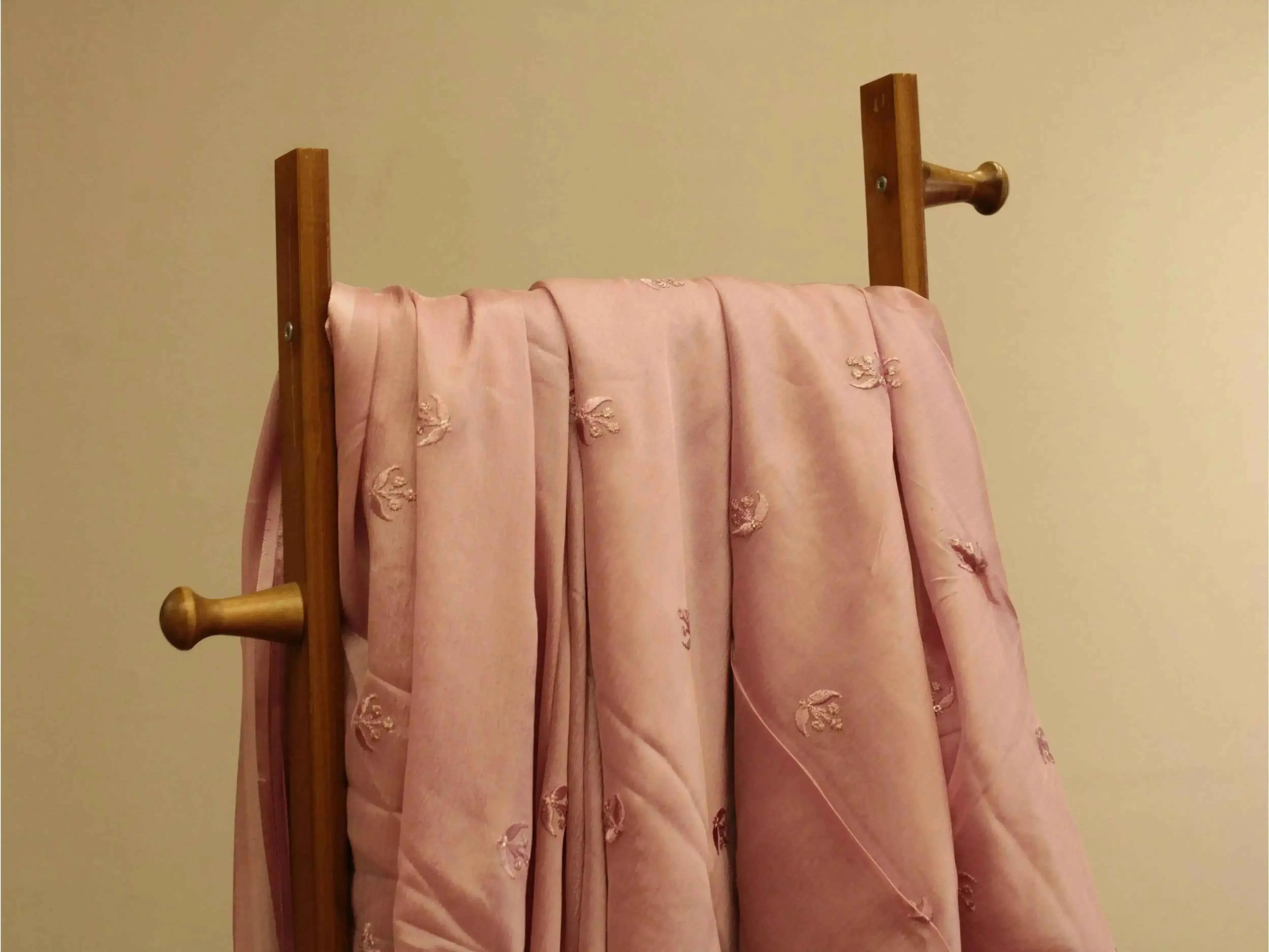 Pure chinon lavender pink fabric with minimal buti embroidery draped on wooden rack