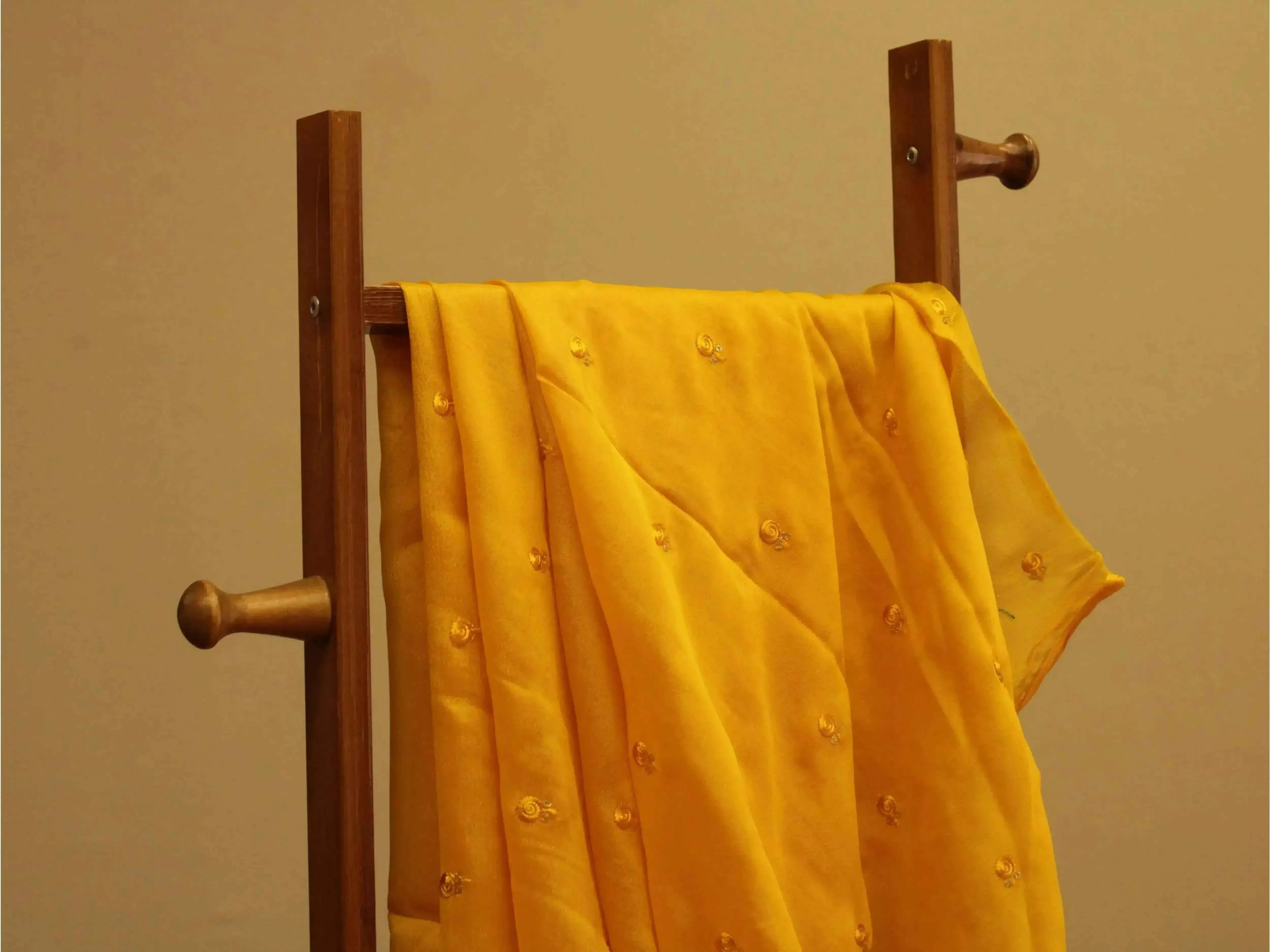 Mustard yellow pure chinon fabric with minimal buti embroidery draped on a wooden stand