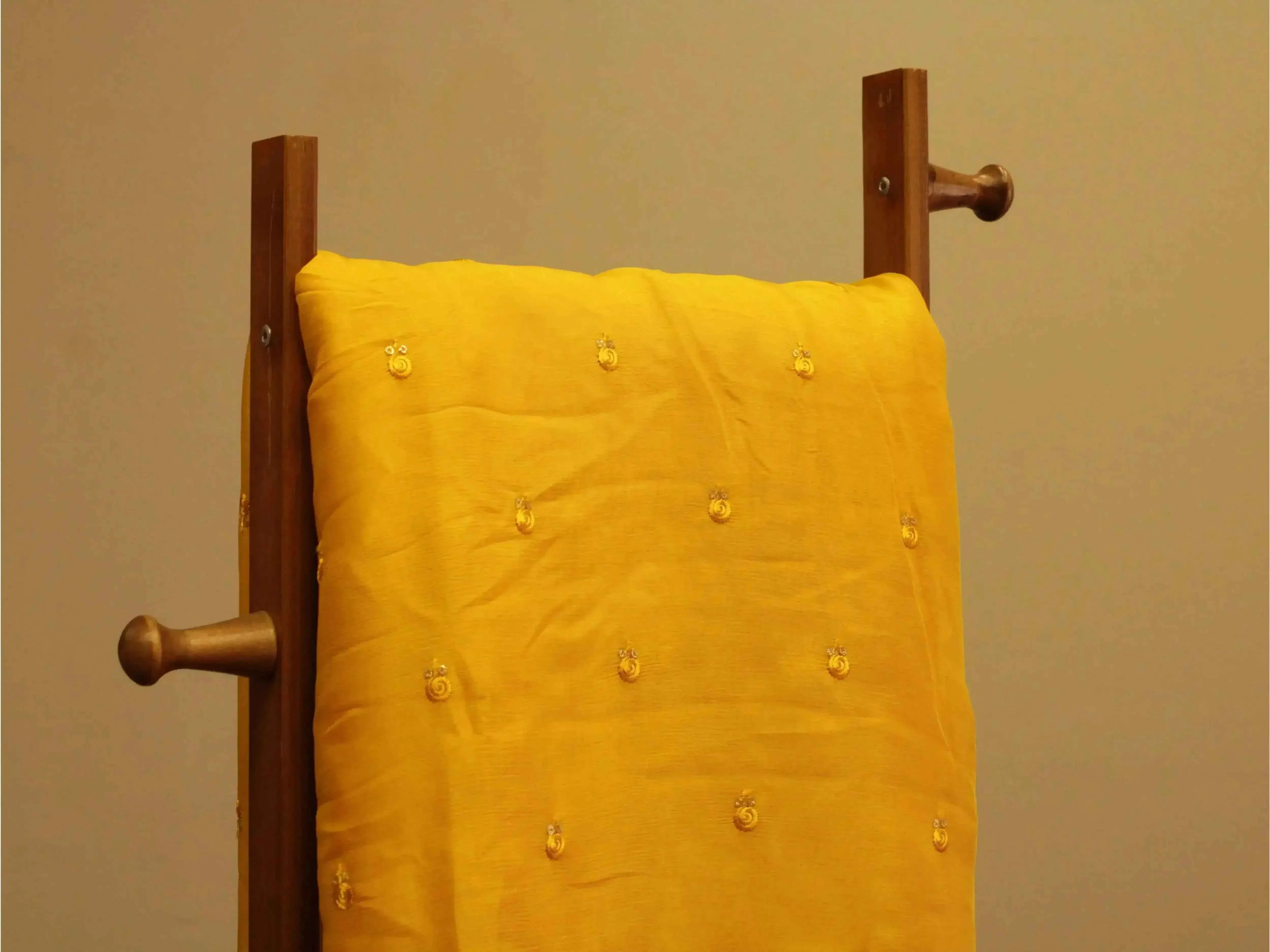 Mustard yellow pure chinon fabric with minimal buti embroidery draped on a wooden hanger