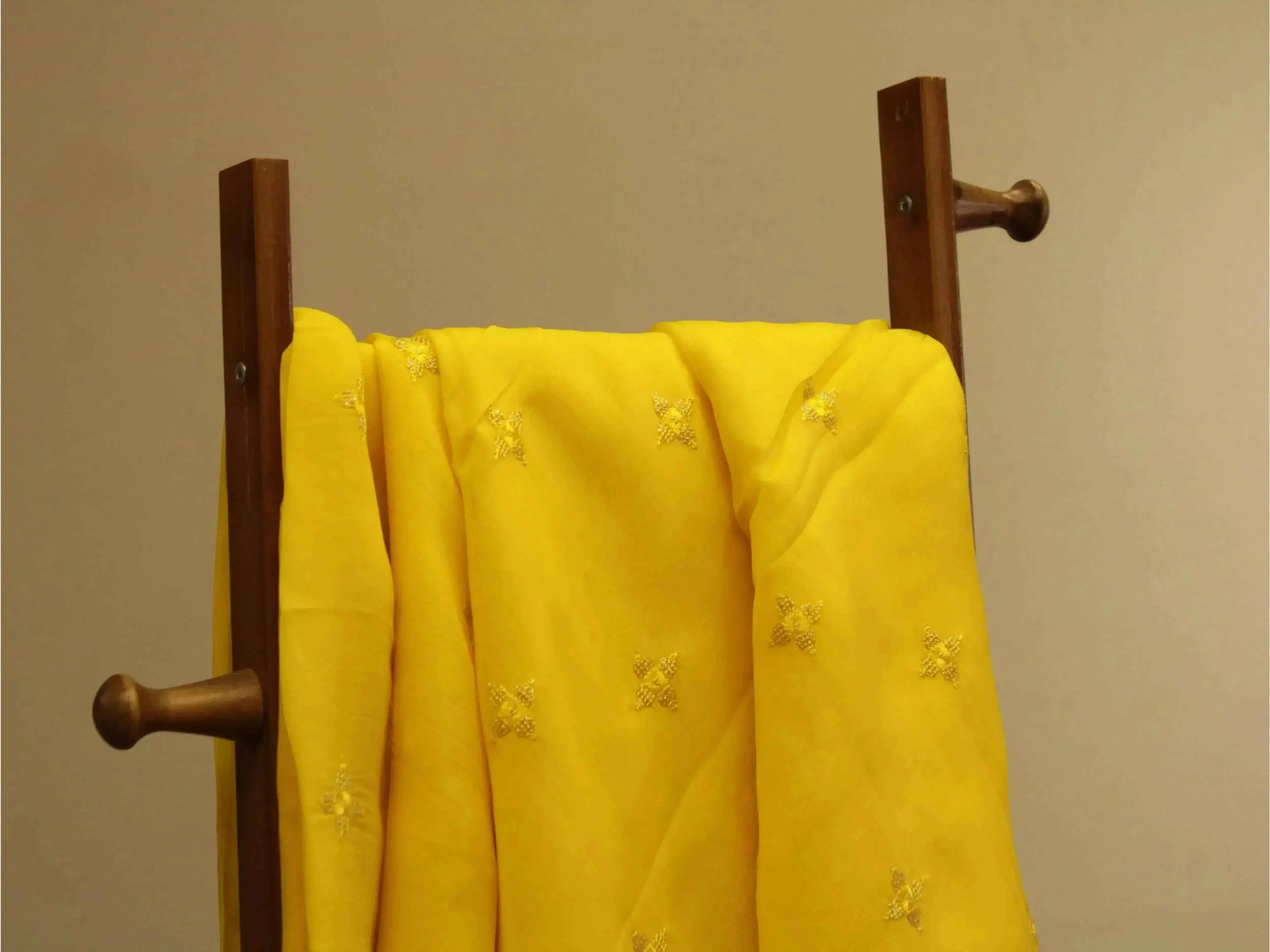 Yellow Chinon fabric with minimal buti embroidery draped on a wooden stand