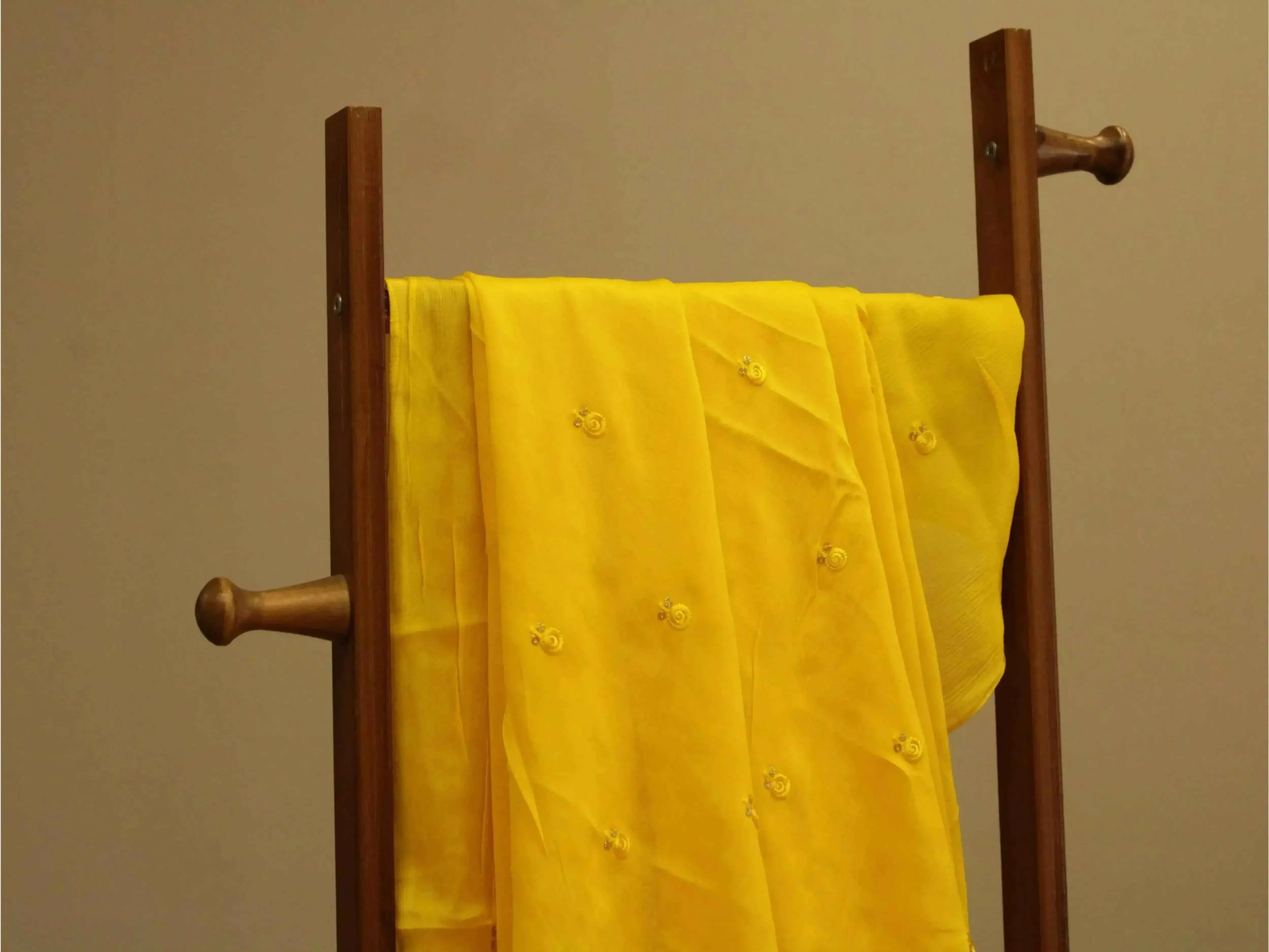 Pure chinon yellow fabric with minimal buti work draped on a wooden stand