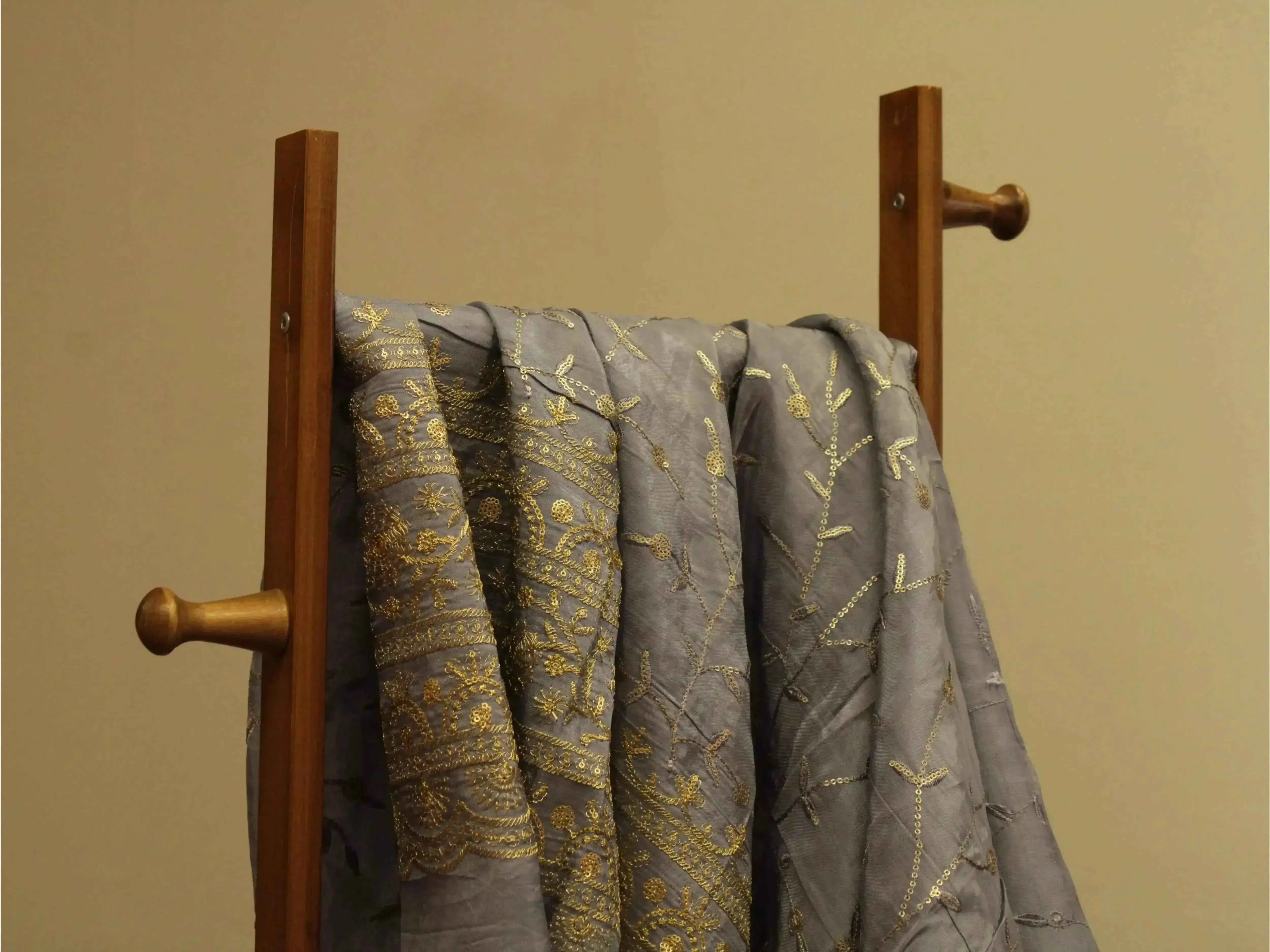 Grey Upada silk fabric with intricate gold embroidery draped on a wooden stand