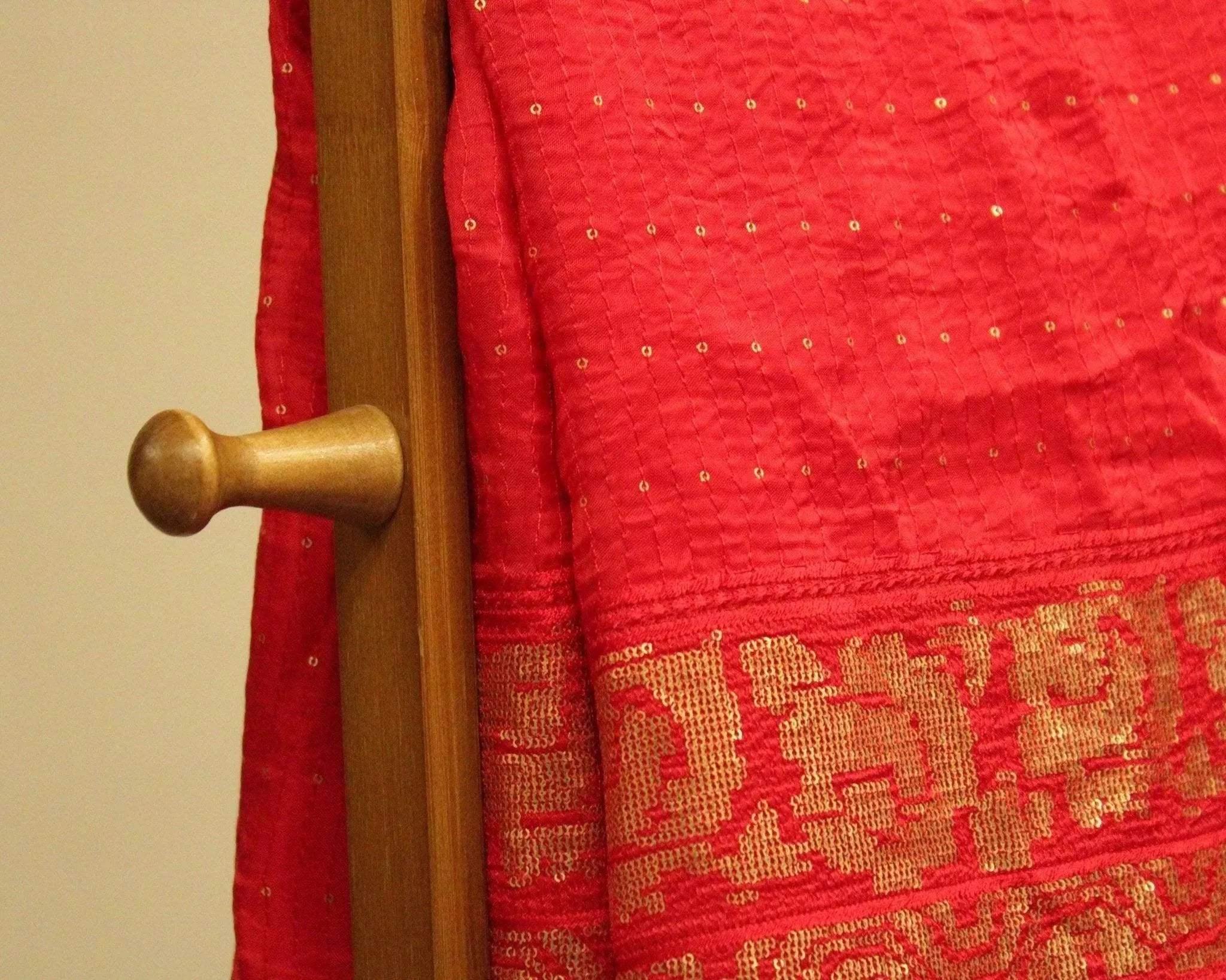 Red upada silk fabric with gold micro work and intricate border pattern draped on a hanger