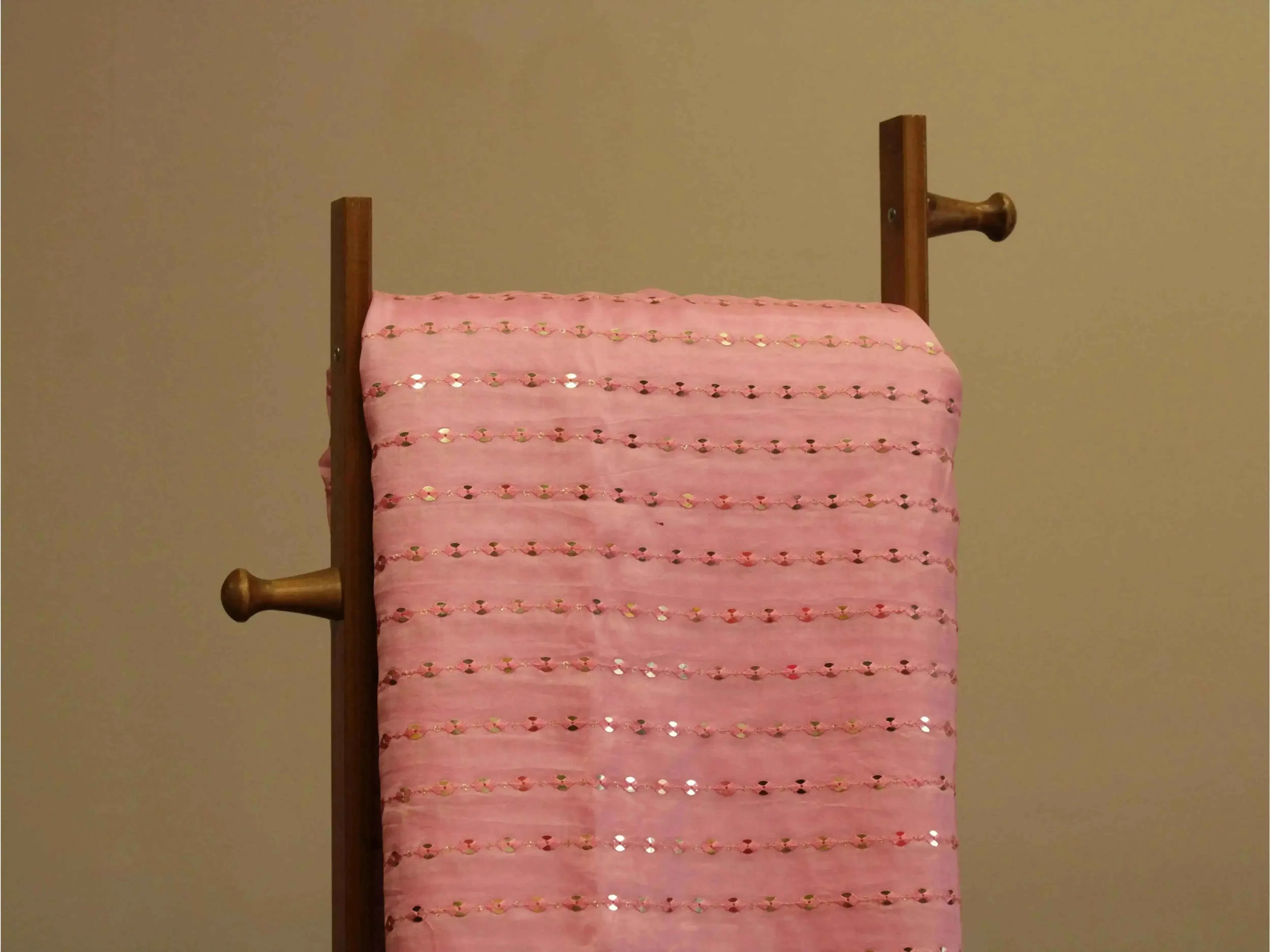 Pink mirror work fabric with sequin embroidery draped on a wooden stand