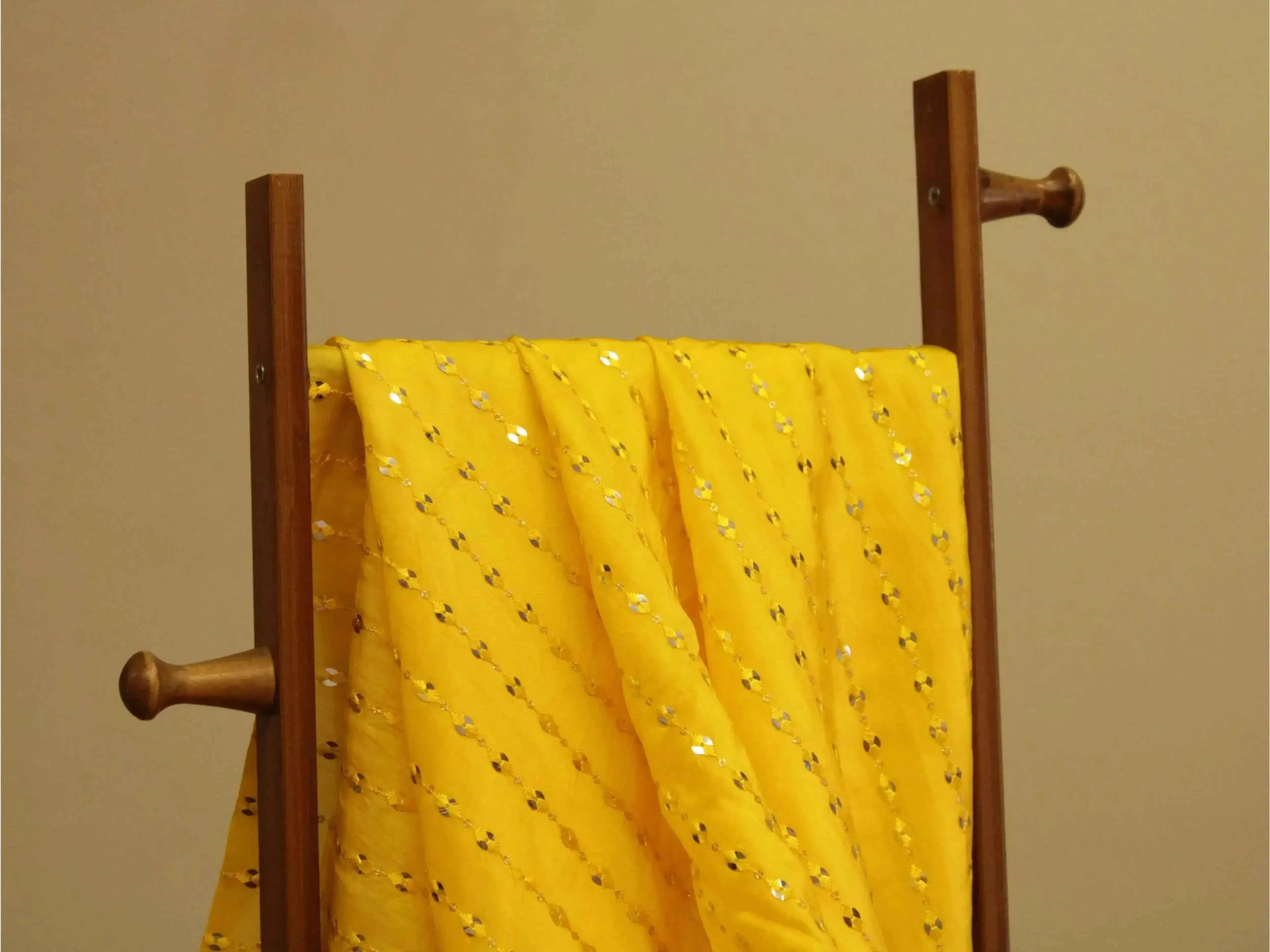 Yellow mirror work fabric with sequin embroidery draped on a wooden stand