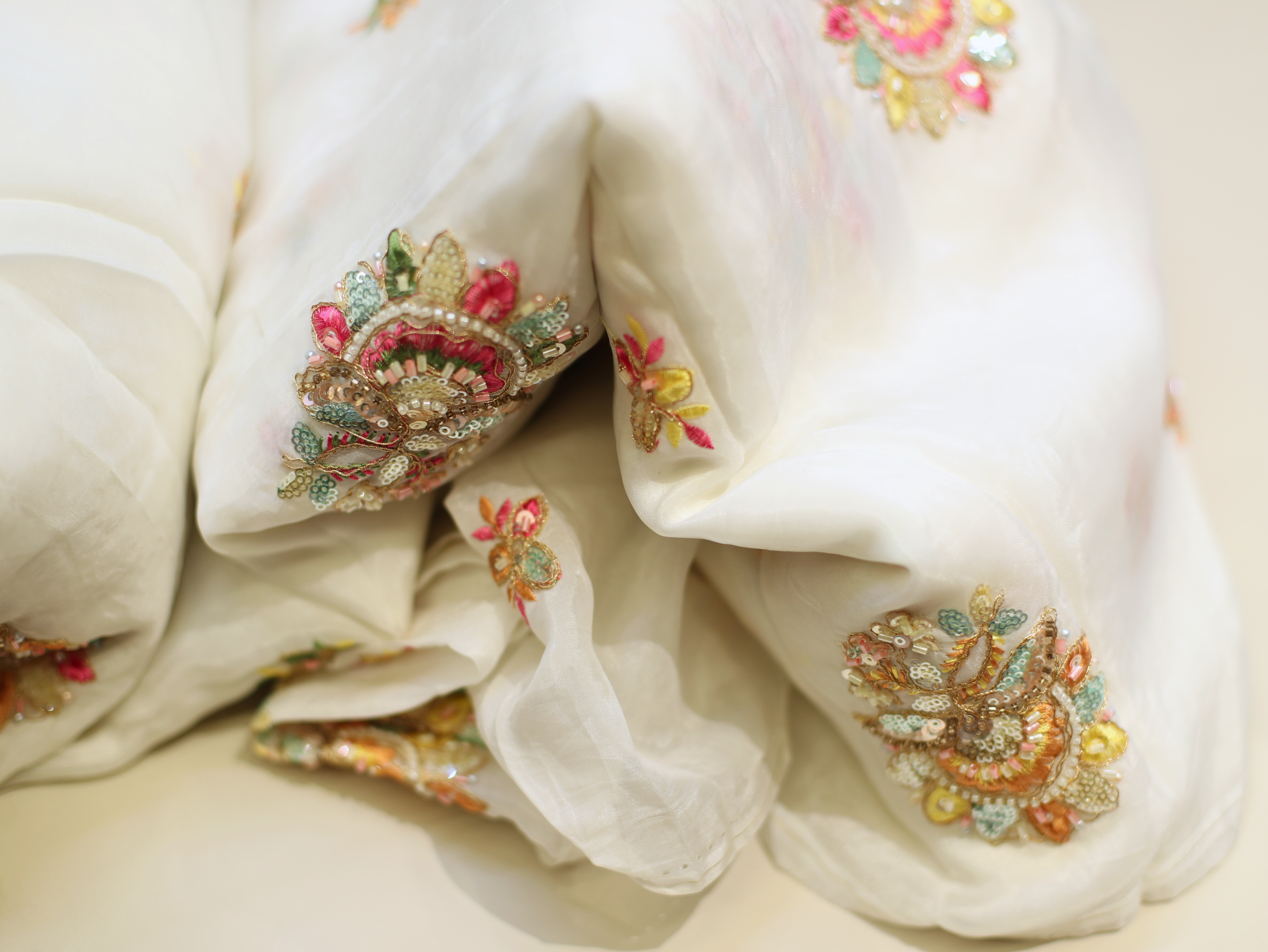 White silk-look fabric with colorful floral embroidery and sequins, Indian textile detail