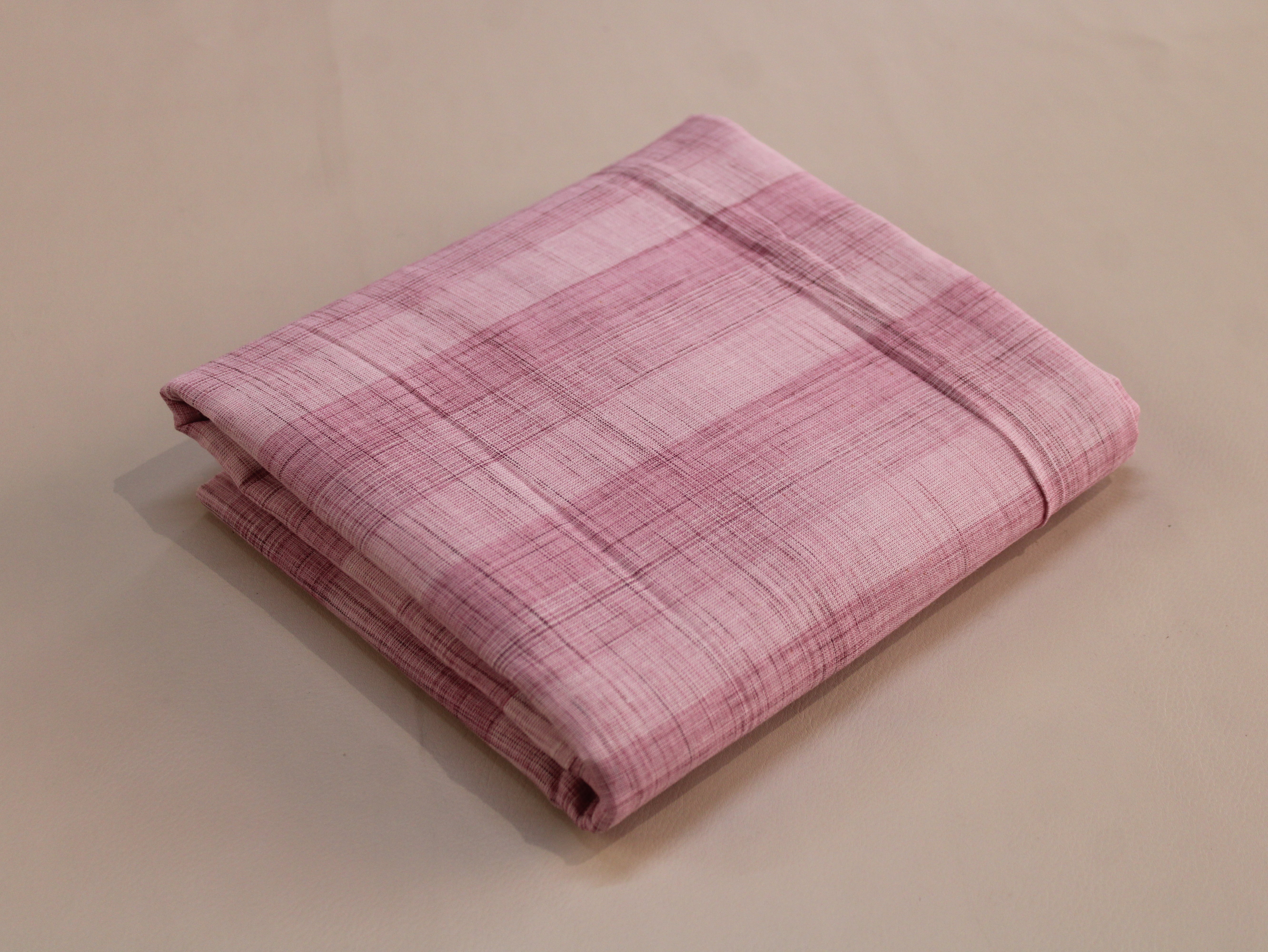 A folded pink plaid fabric, likely a tablecloth or napkin, displayed on a neutral beige background.